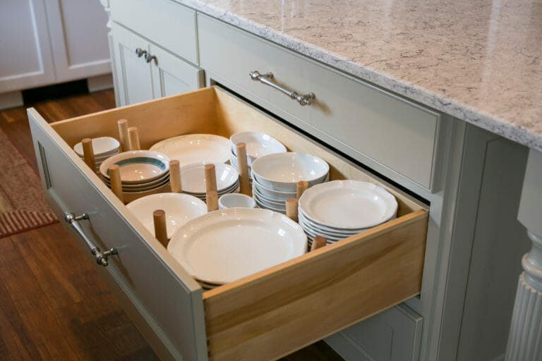 Open drawer with pegboard plate storage system holding white ceramic dinnerware, part of a custom kitchen design by interior designers in Madison WI.