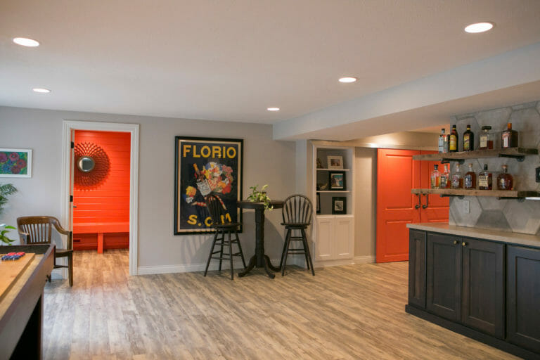 Basement bar area featuring rustic wood shelving, a vibrant orange door, and cozy seating with eclectic decor.