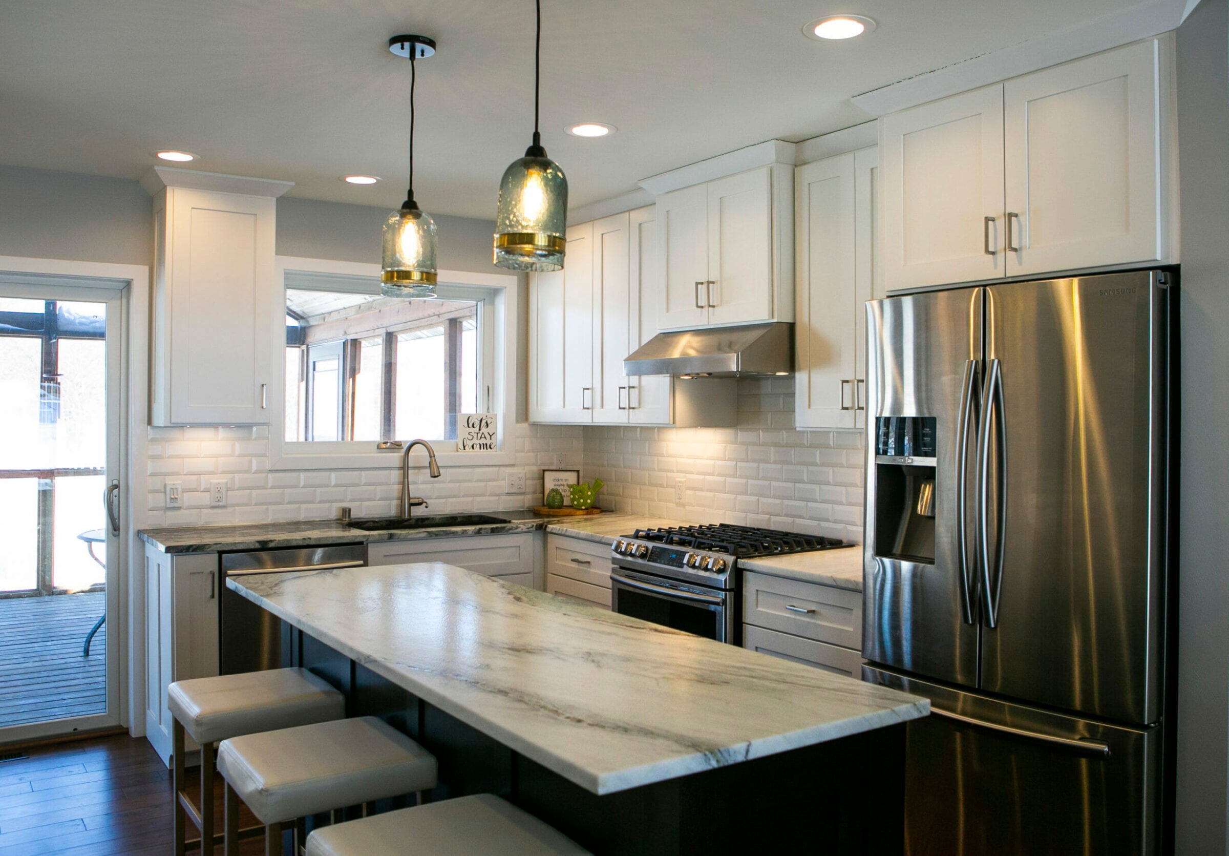 Modern kitchen featuring white cabinets, stainless steel appliances, a marble island, and pendant lighting.
