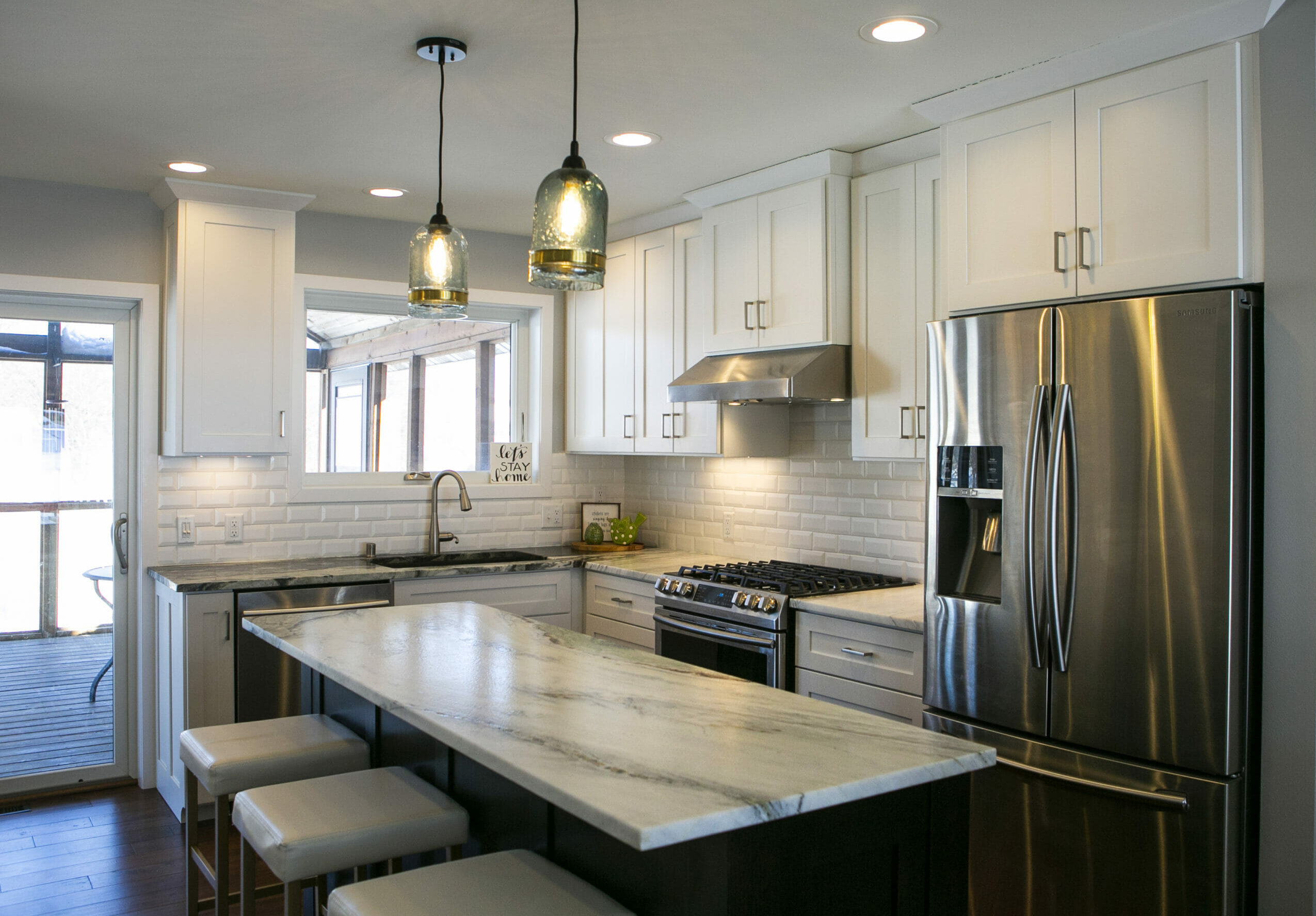 Modern kitchen featuring white cabinets, stainless steel appliances, a marble island, and pendant lighting.