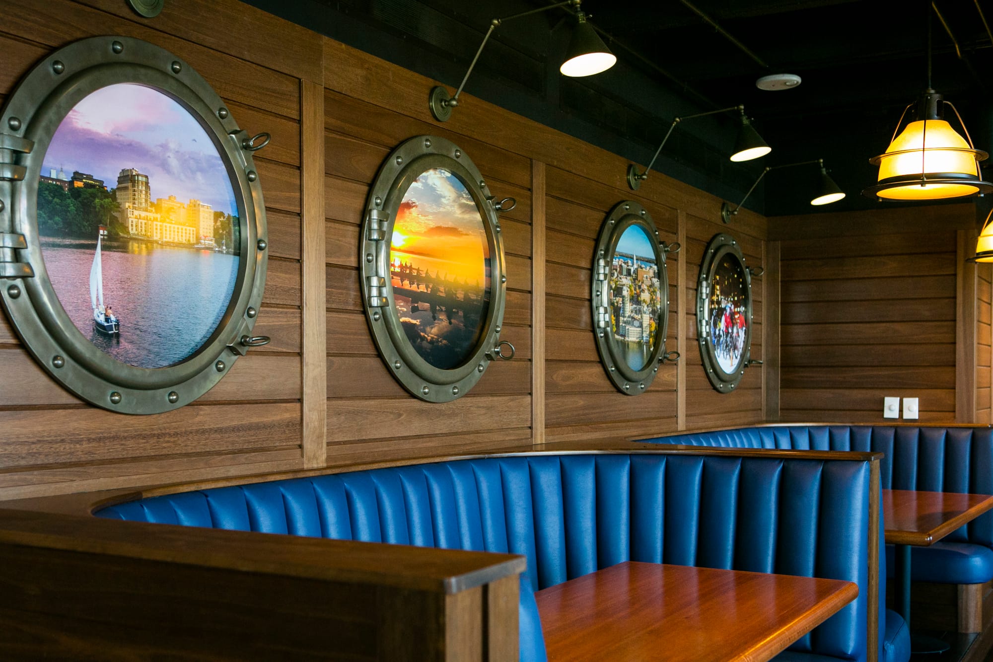 Stylish restaurant interior design in Madison, WI, featuring nautical-inspired décor with porthole wall art, rich wood paneling, and plush blue booth seating. Designed by top interior designers and home remodeling contractors in Madison for a unique dining experience.