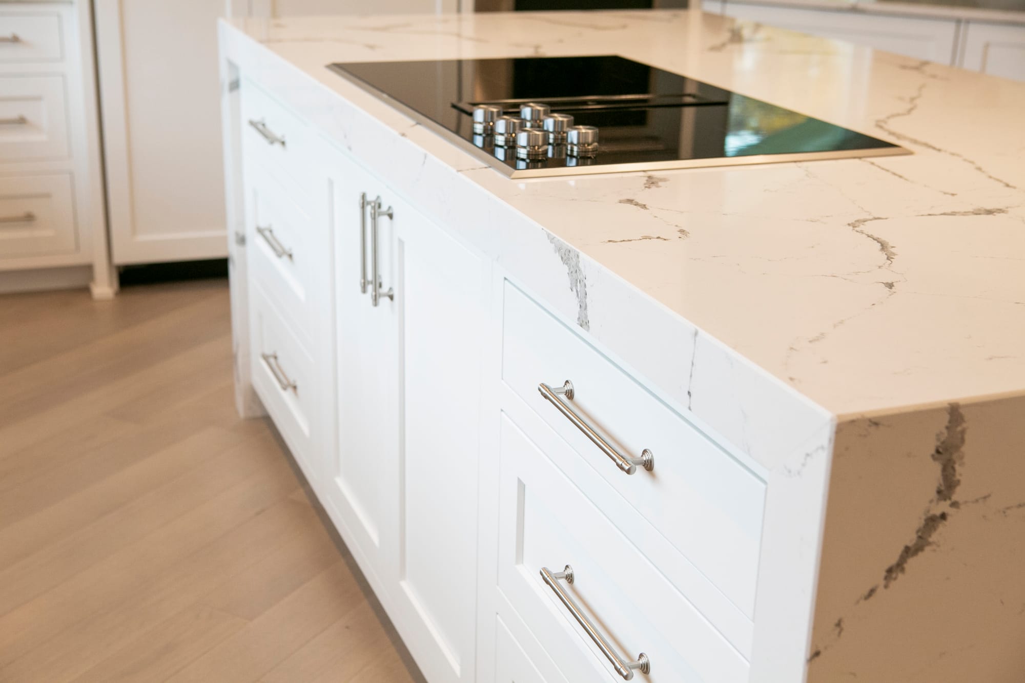 Close-up of a modern kitchen island featuring a sleek white quartz countertop with elegant veining, custom cabinetry, and a built-in cooktop. Designed by top interior designers in Madison, WI, this kitchen remodel blends functionality with contemporary aesthetics. Ideal for homeowners seeking kitchen renovations, home remodeling, and interior design services in Madison, WI.