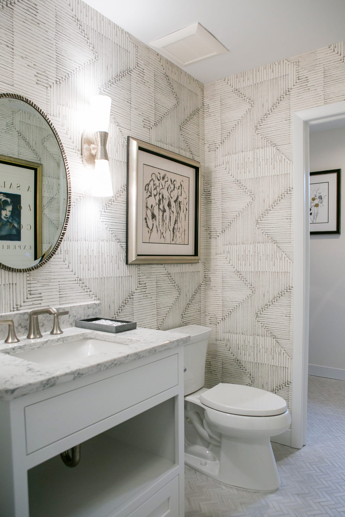 Stylish bathroom featuring a marble vanity, patterned wallpaper, framed art, and modern lighting.