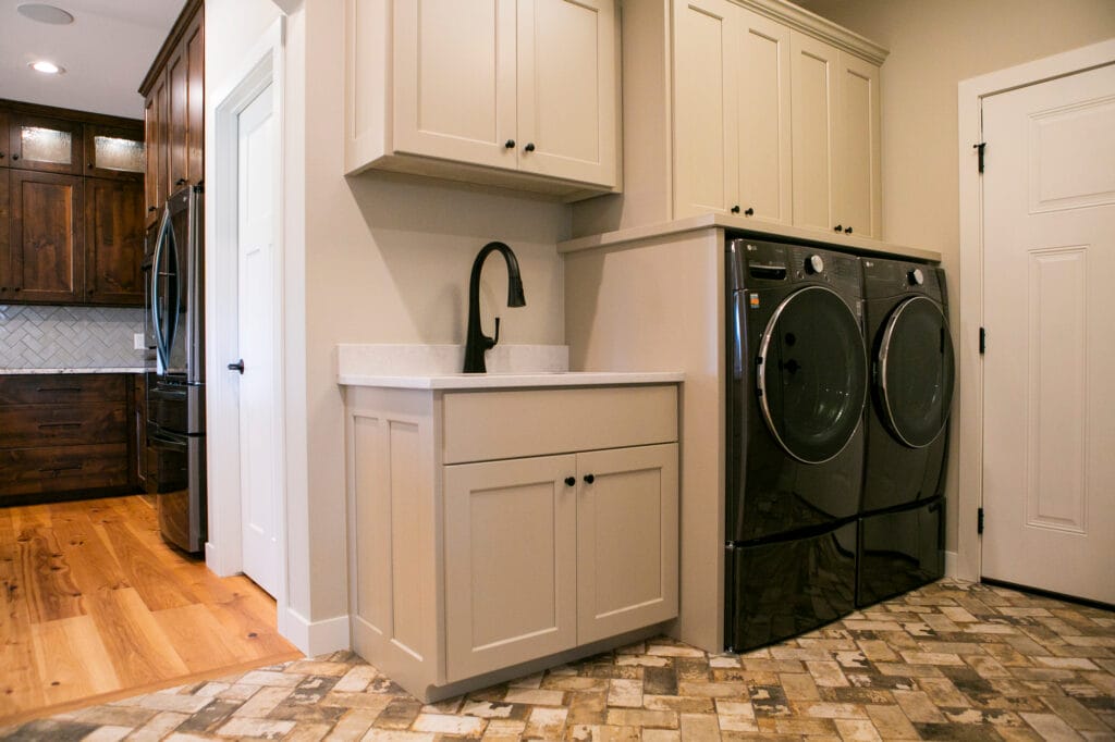A stylish and functional laundry room remodel in Madison, WI, featuring custom beige cabinetry, a sleek black faucet, quartz countertops, and high-end LG washer and dryer units. The space is designed for efficiency with ample storage and a dedicated sink area. Expertly crafted by leading home remodeling contractors in Madison, WI, specializing in modern interior design and home renovations.