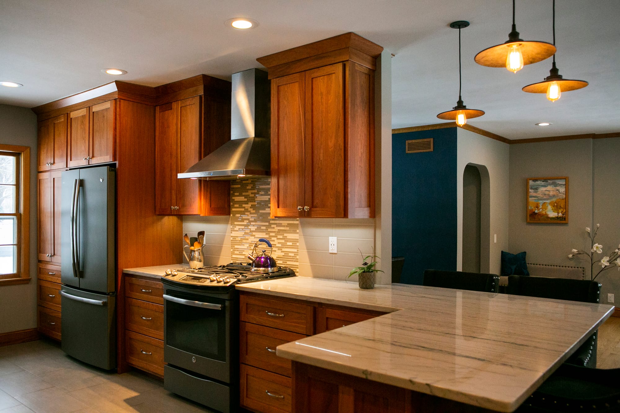 Open concept kitchen featuring custom wood cabinets, a large marble island, mosaic tile backsplash, and pendant lighting, designed by interior designers in Madison WI for a full home renovation.