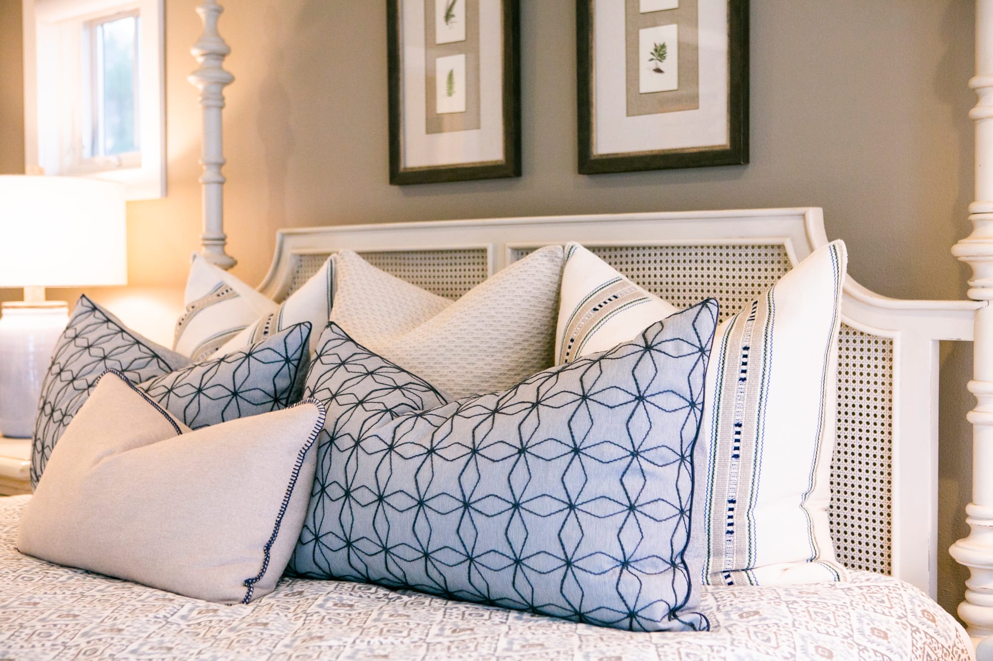 White cane four poster bed with blue and white bedding, large white ceramic lamp with white shade