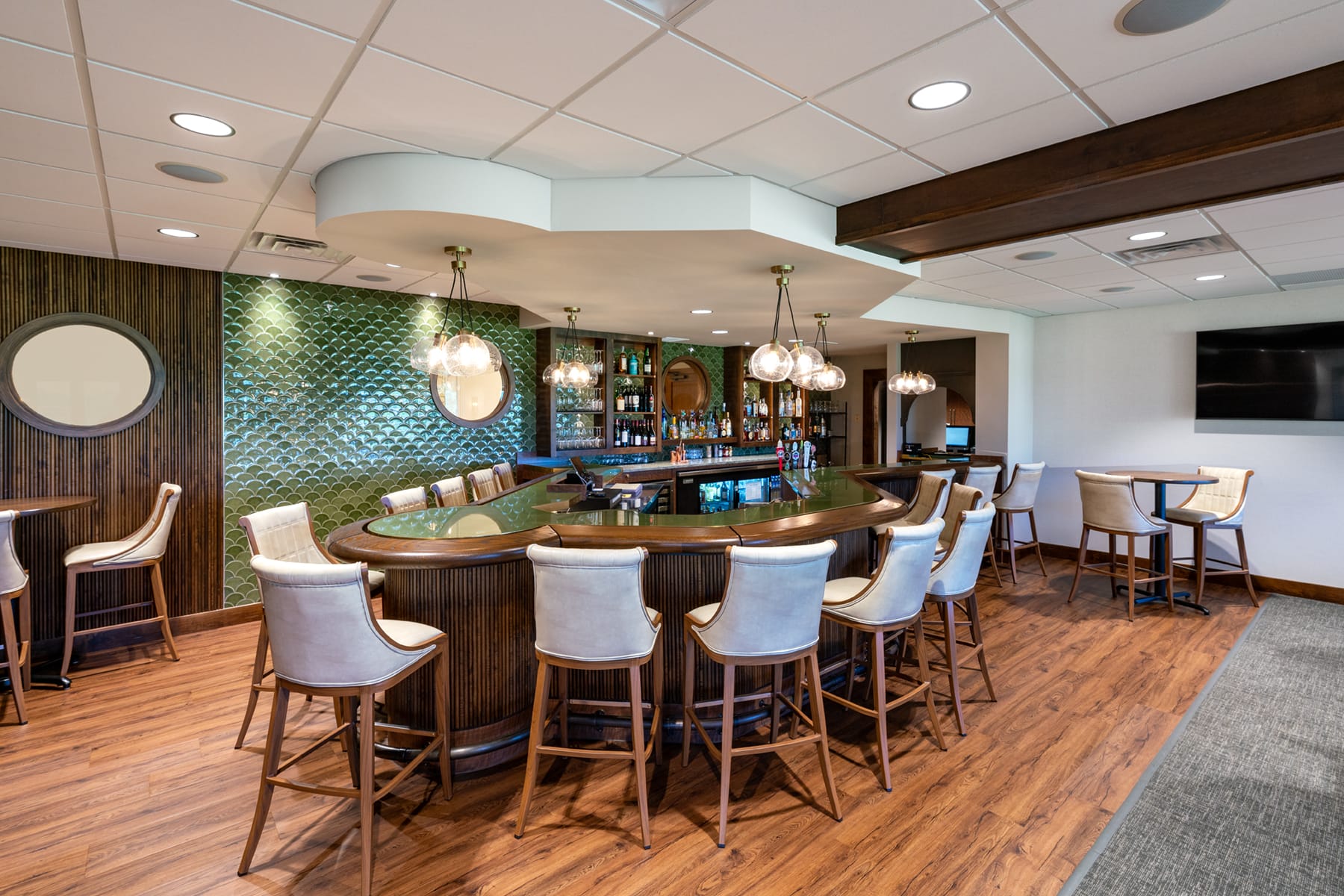 Art deco green and deep wooden bar. The shape of the bar is unique and is accompanied by white leather chairs. The bar backsplash is scalloped green.