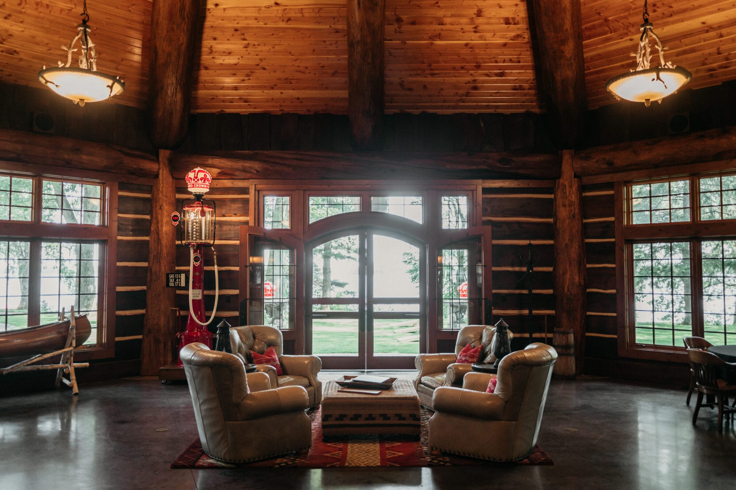 Cozy log cabin interior featuring leather armchairs, a wooden table, and large windows overlooking a serene outdoor view.