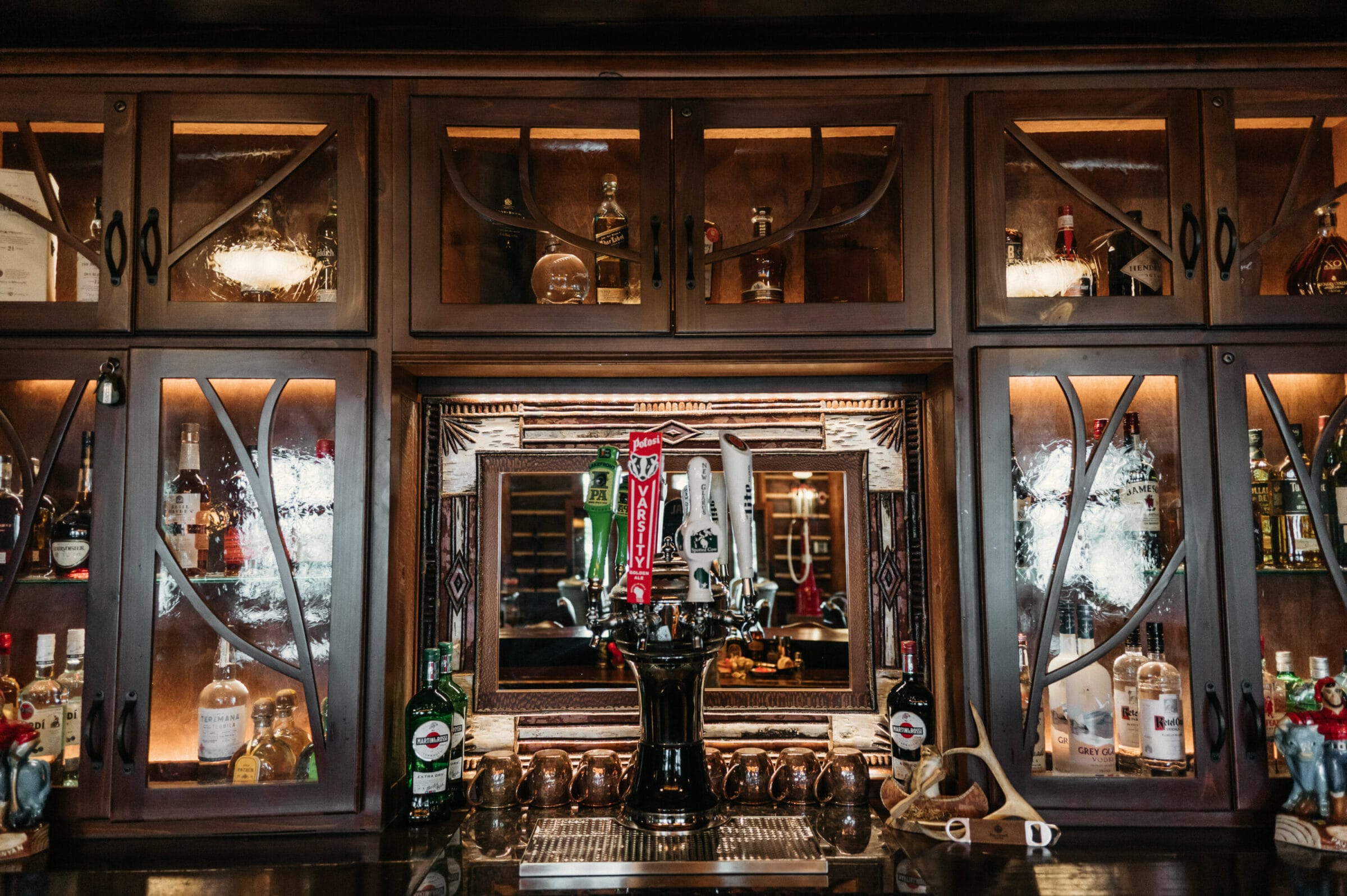 Elegant wooden bar with illuminated shelves displaying various liquor bottles and a prominent beer tap in the center.