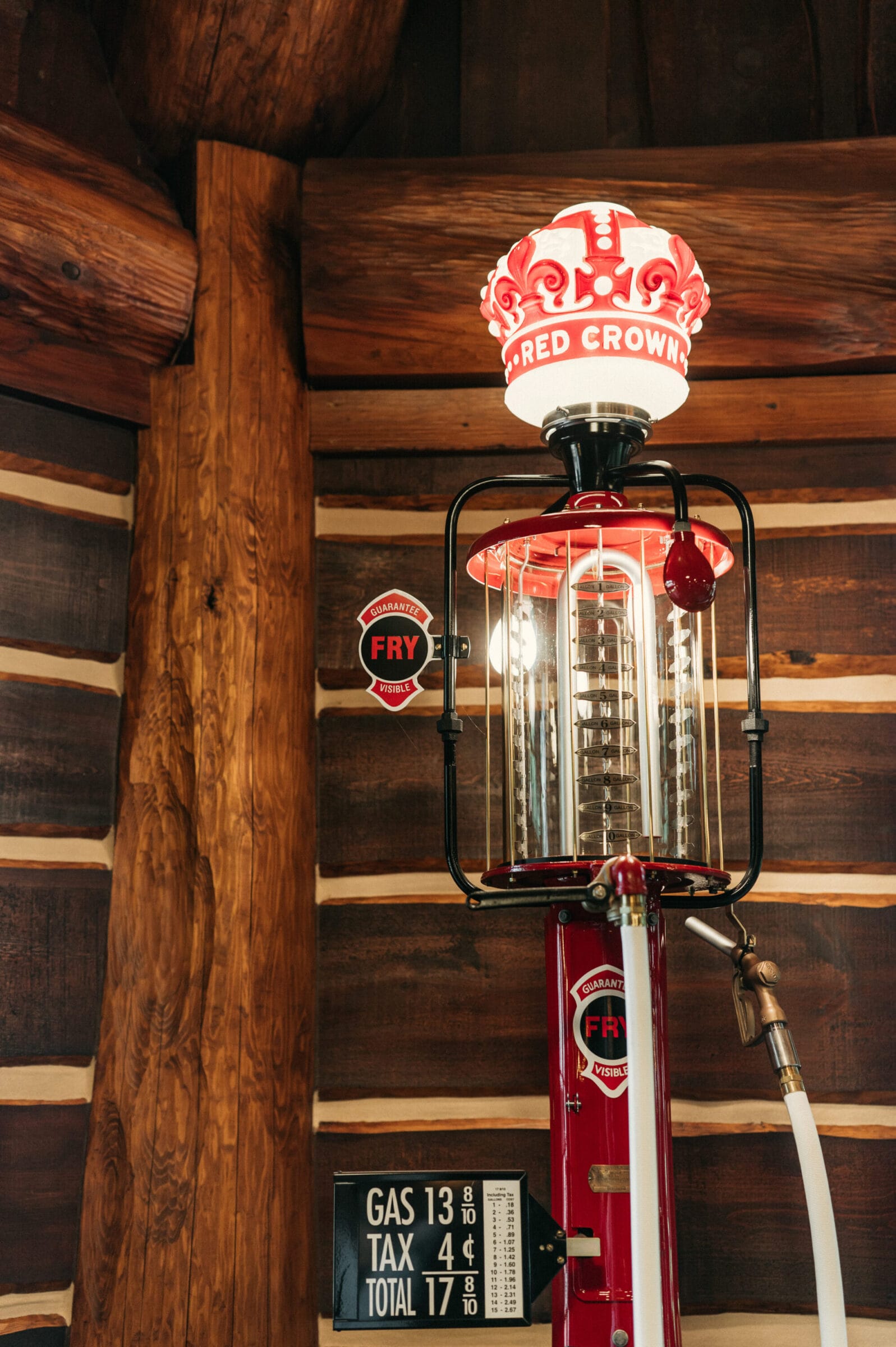 Vintage gas pump with a red crown light, surrounded by wooden logs and a price board displaying gas and tax rates.