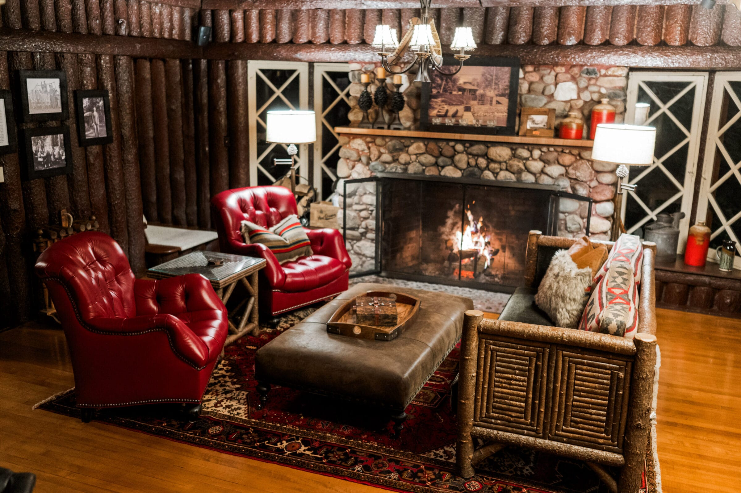 Cozy living room with red leather chairs, a stone fireplace, and rustic decor, illuminated by warm lighting.