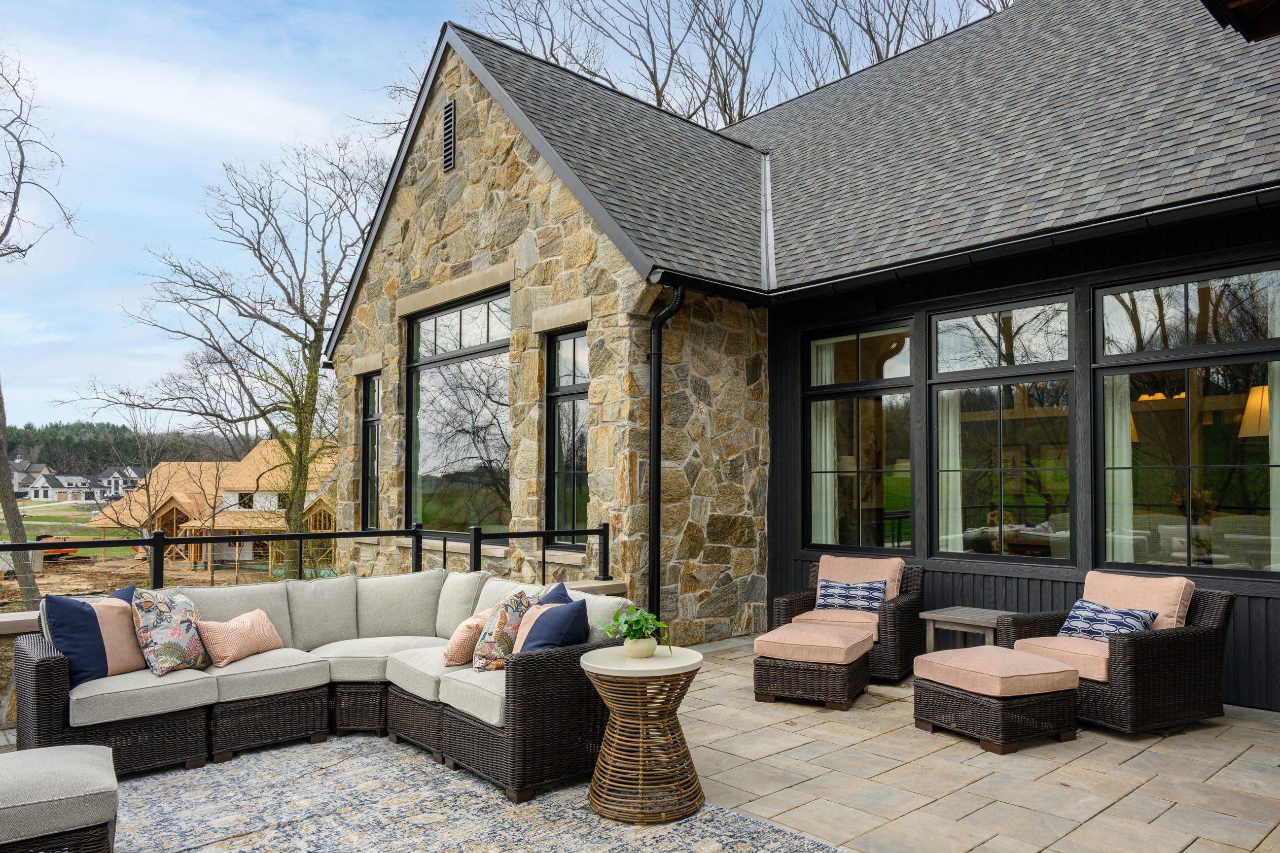 Stylish outdoor seating area with a stone wall, plush cushions, and a scenic view of trees and nearby homes.