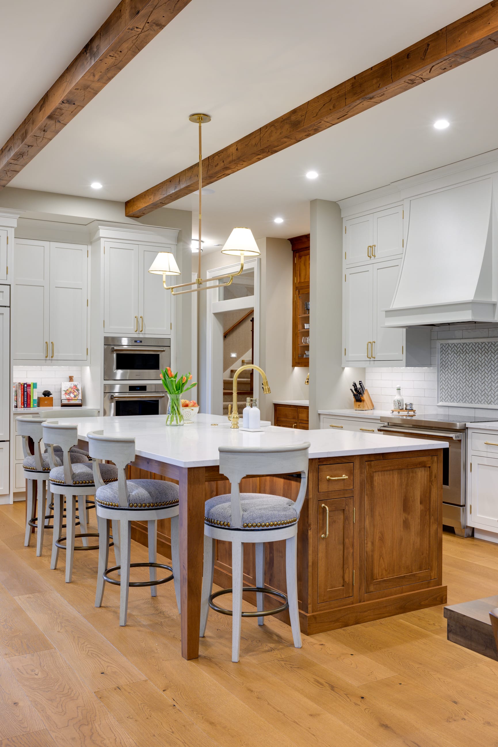 Modern kitchen featuring a large island with bar stools, white cabinetry, wooden beams, and stylish lighting.