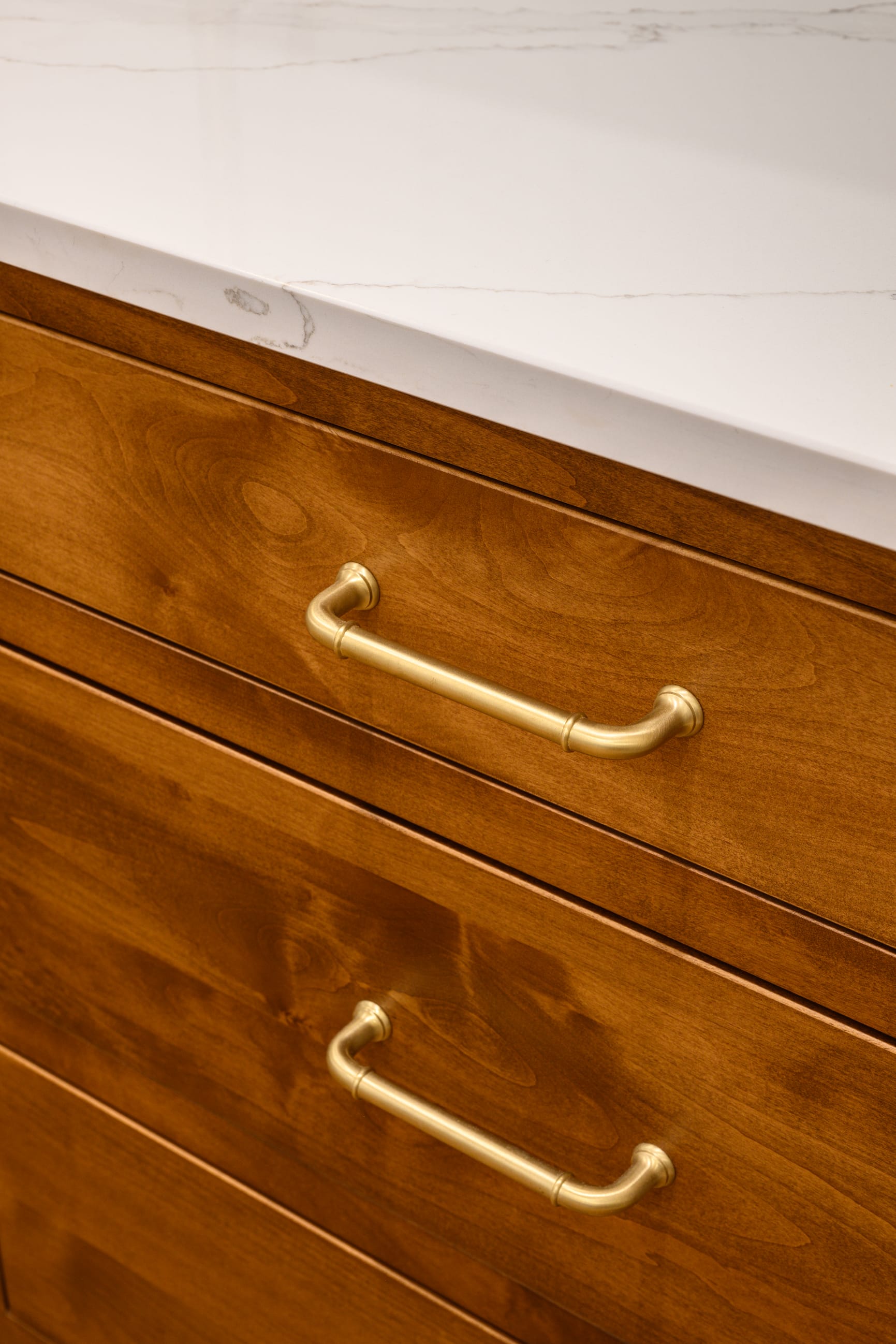 Wooden drawers with brass handles, topped by a white marble countertop featuring subtle veining.