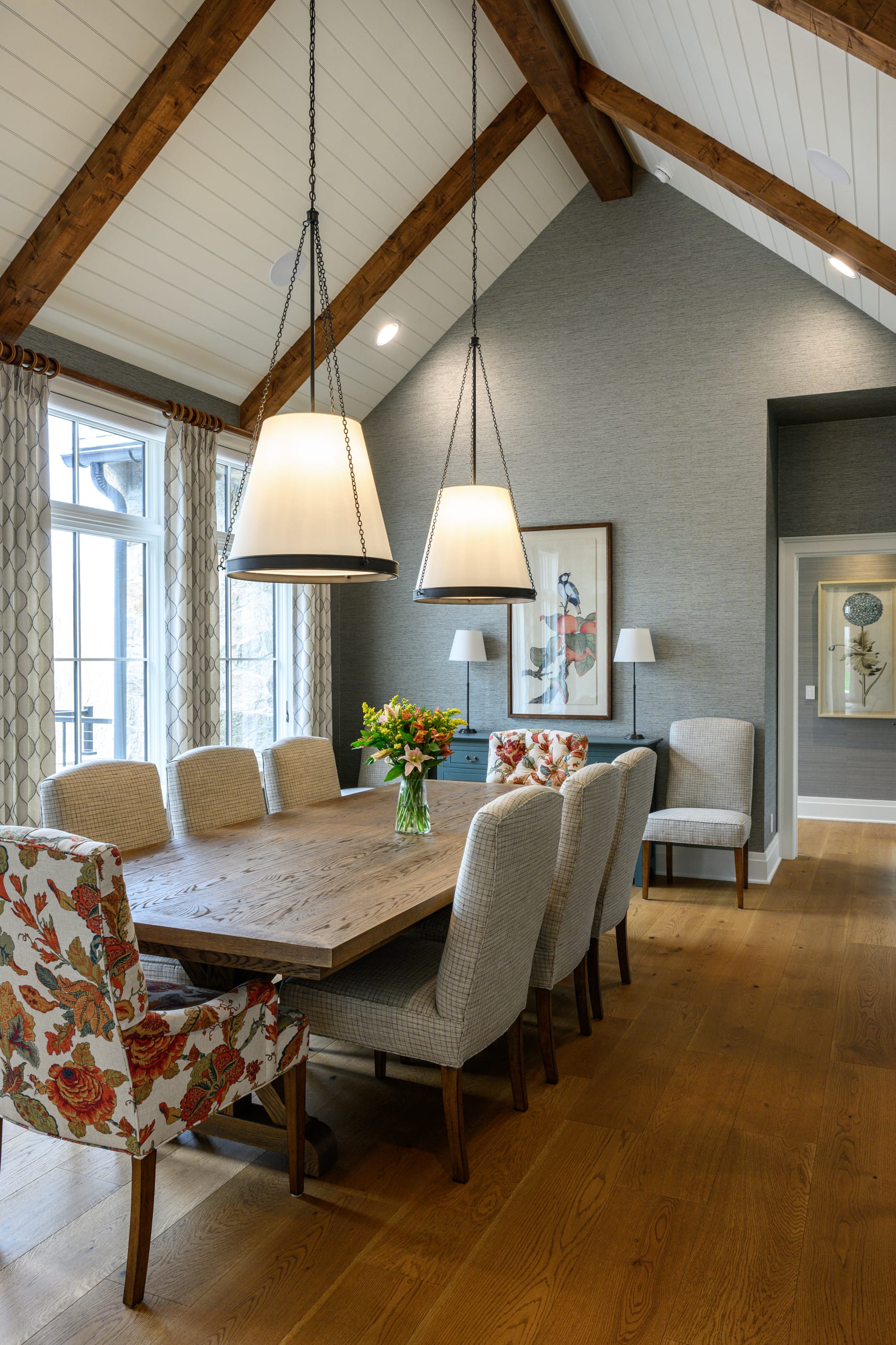 Bright dining area featuring a wooden table, upholstered chairs, and large pendant lights under a vaulted ceiling.