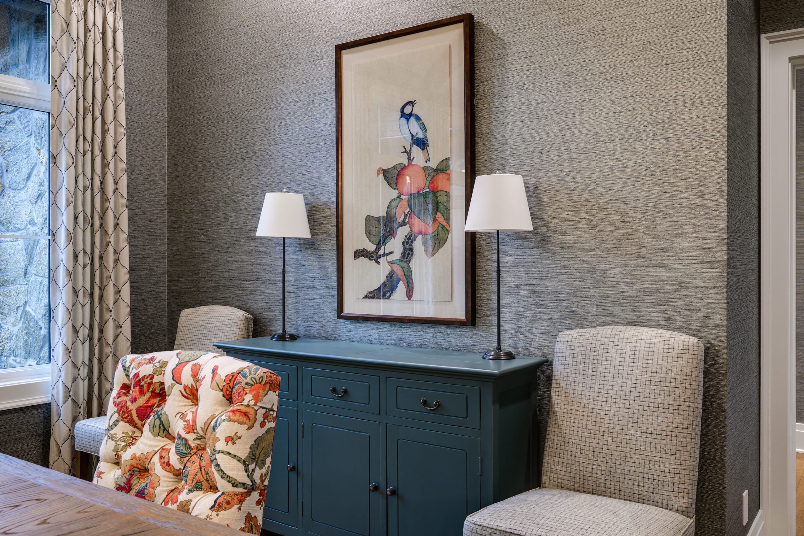 Stylish room featuring a blue cabinet, floral chair, and a bird-themed artwork, complemented by two table lamps.