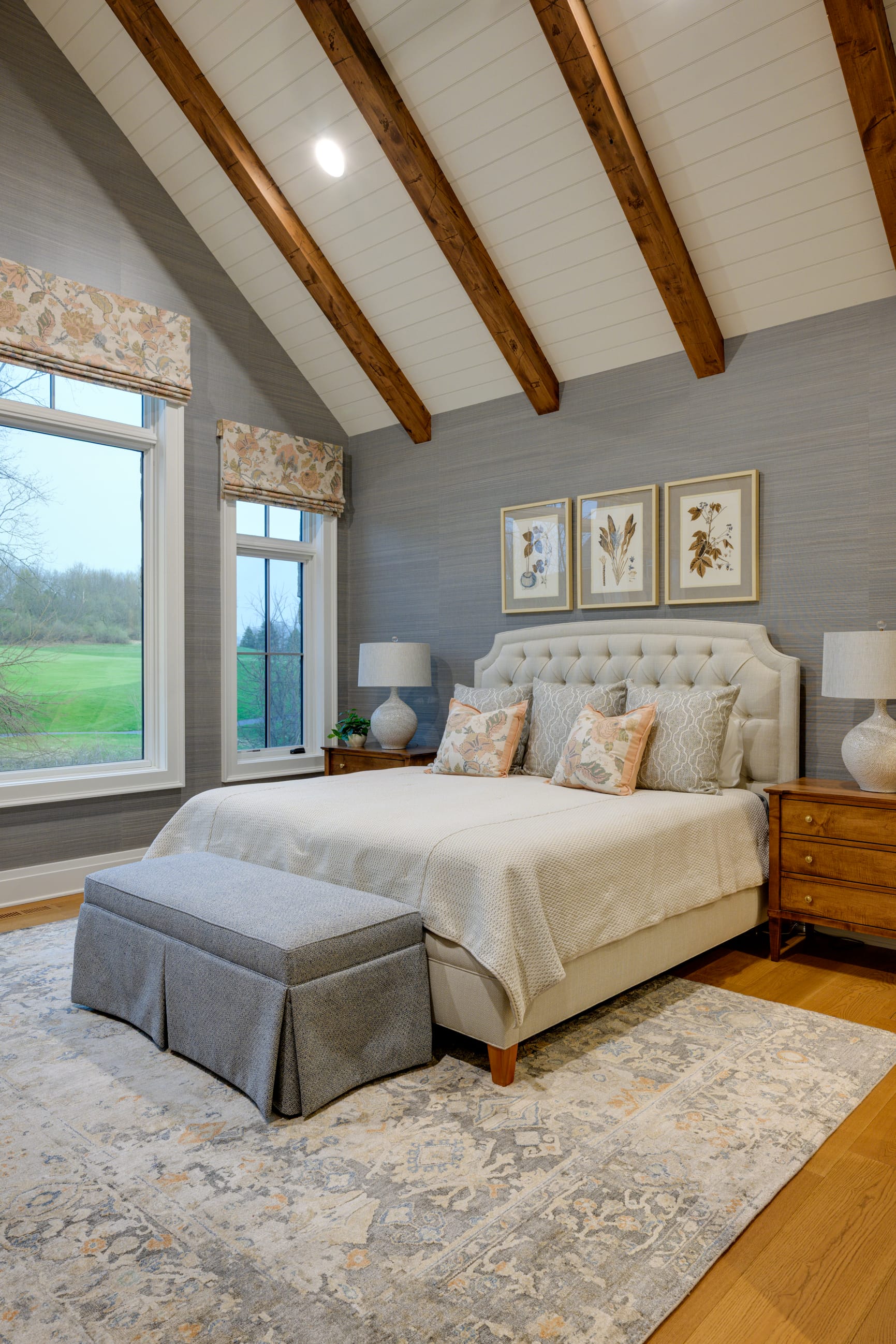 Cozy bedroom featuring a tufted bed, decorative pillows, wooden furniture, and large windows with scenic views.