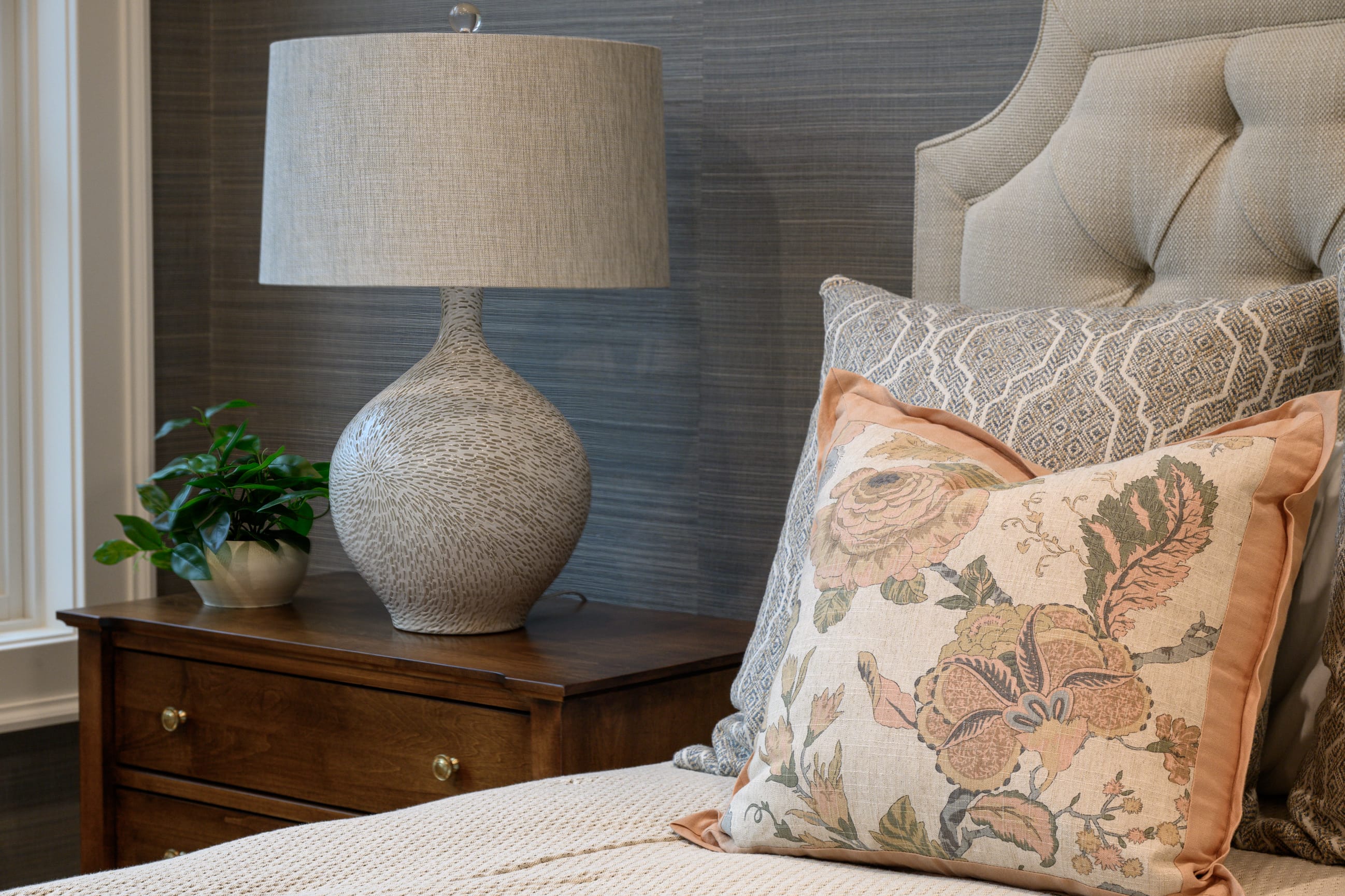 Cozy bedroom corner featuring a textured lamp, decorative pillows, and a small potted plant on a wooden nightstand.