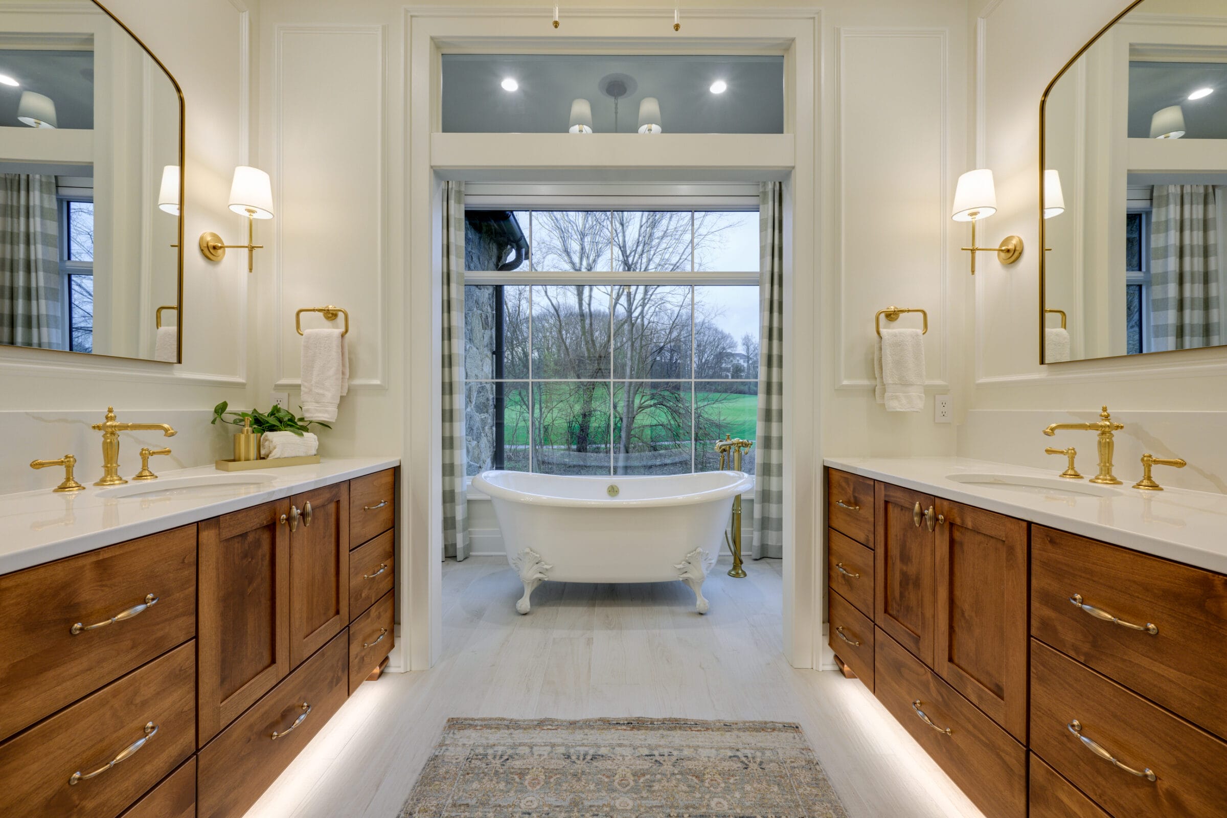 Elegant bathroom featuring dual vanities, a freestanding tub, and large windows with a view of greenery.