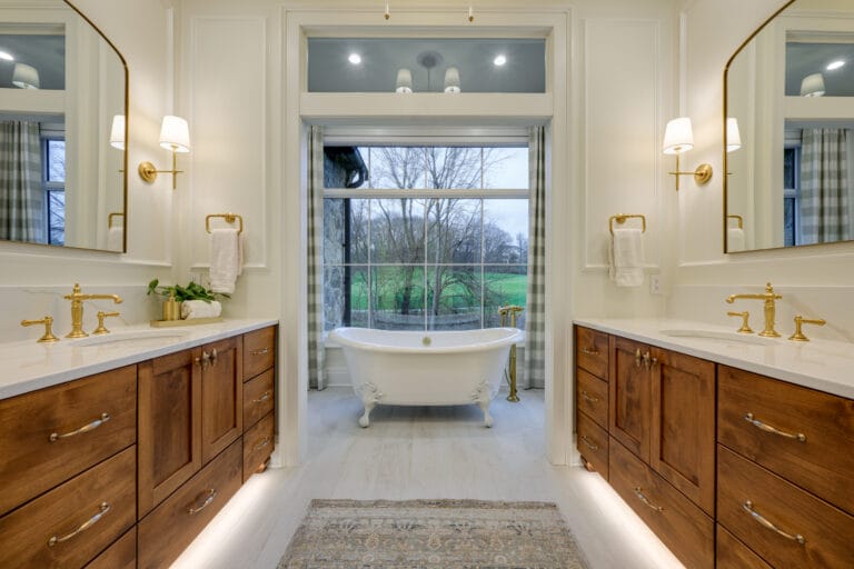 Elegant bathroom featuring dual vanities, a freestanding tub, and large windows with a view of greenery.