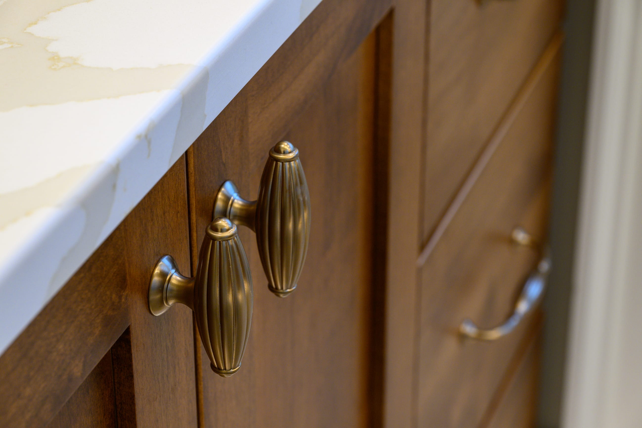 Elegant brass cabinet handles on a wooden cabinet, with a marble countertop featuring subtle veining.