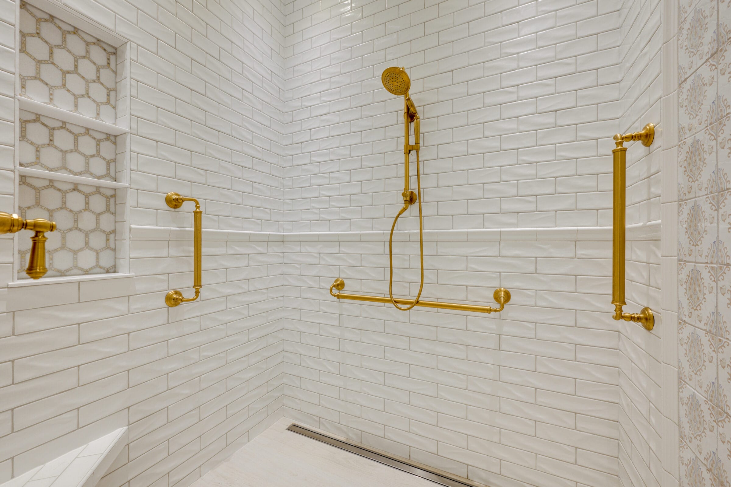 Elegant shower space featuring white subway tiles and gold fixtures, including a handheld showerhead and grab bars.