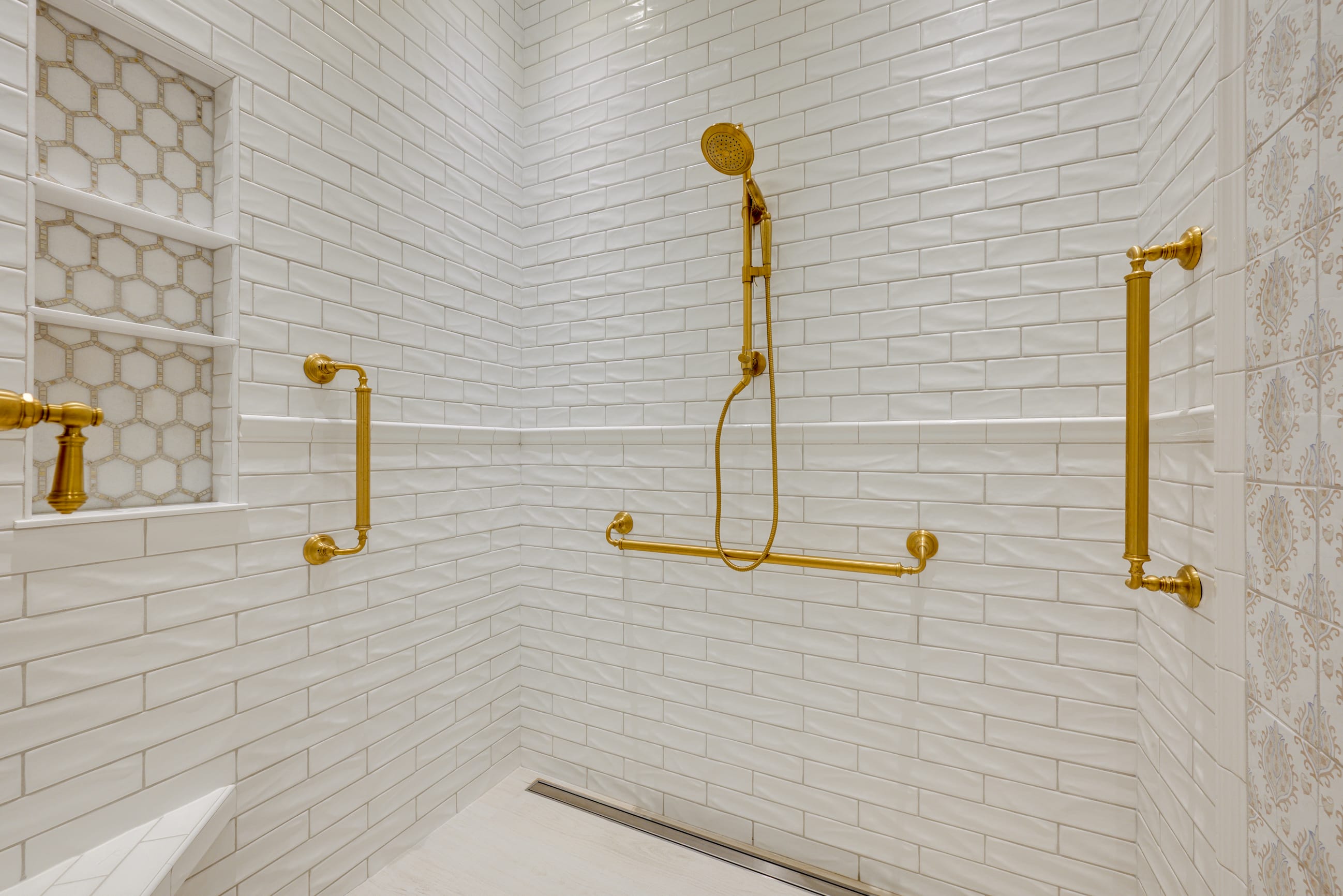Elegant shower space featuring white subway tiles and gold fixtures, including a handheld showerhead and grab bars.