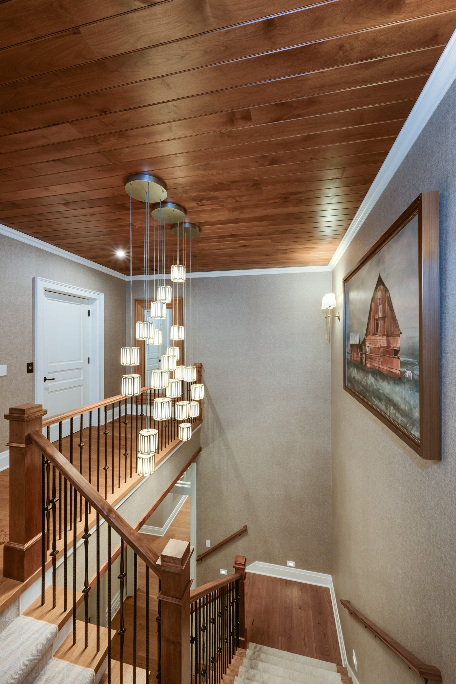 Elegant staircase with wooden railings, modern pendant lights, and a framed painting of a barn on the wall.
