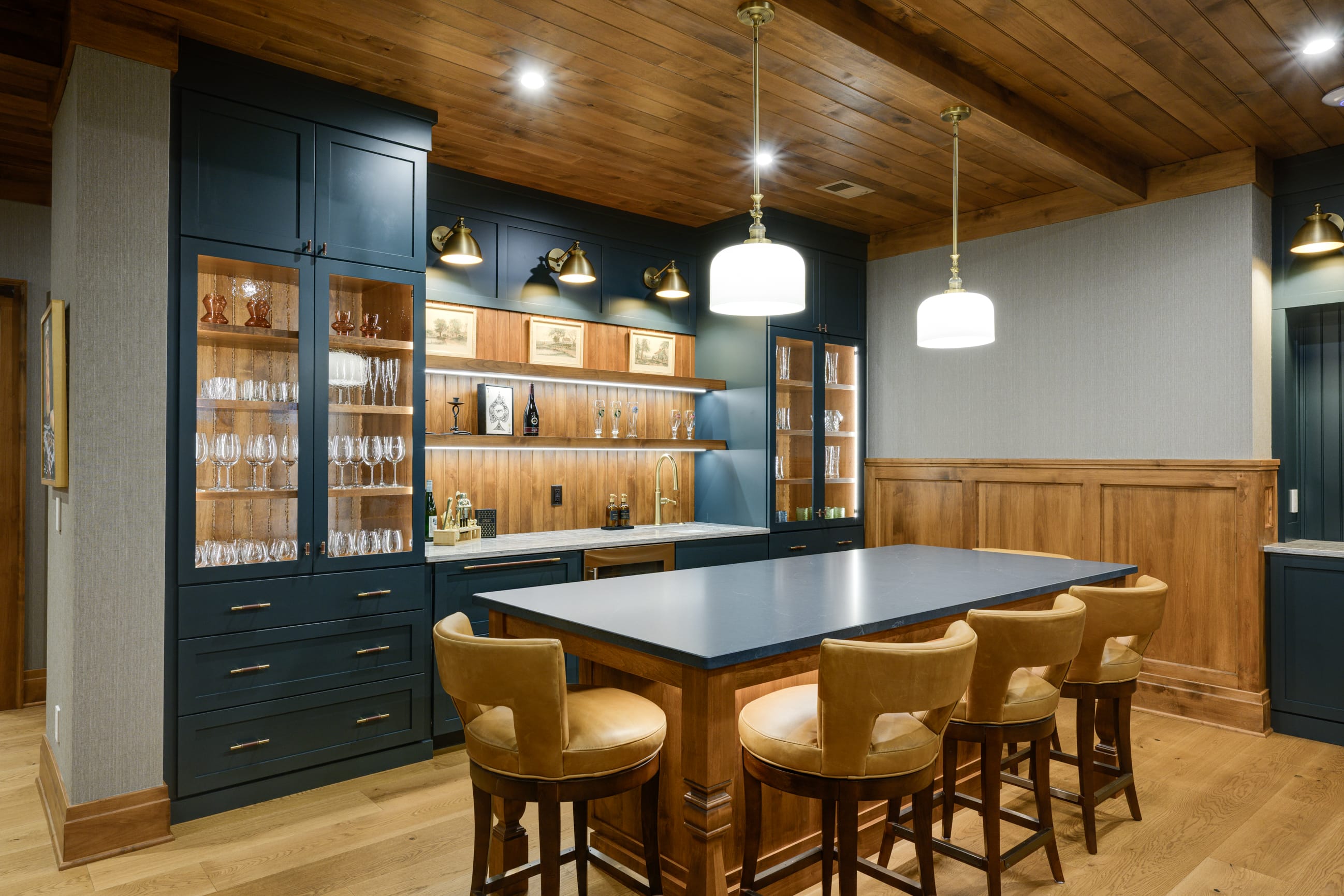 Stylish home bar featuring a dark blue cabinet, wooden accents, glassware display, and leather bar stools.