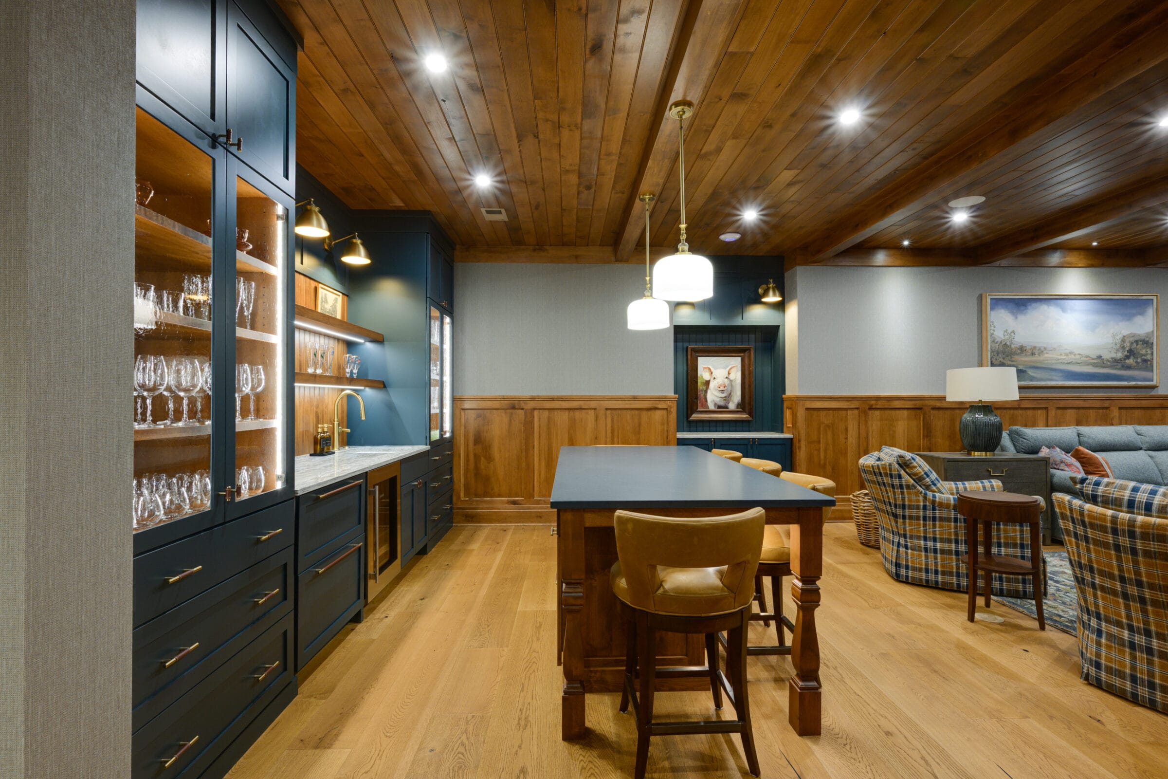 Stylish bar area with blue cabinetry, glassware, wooden accents, and cozy seating featuring plaid patterns.