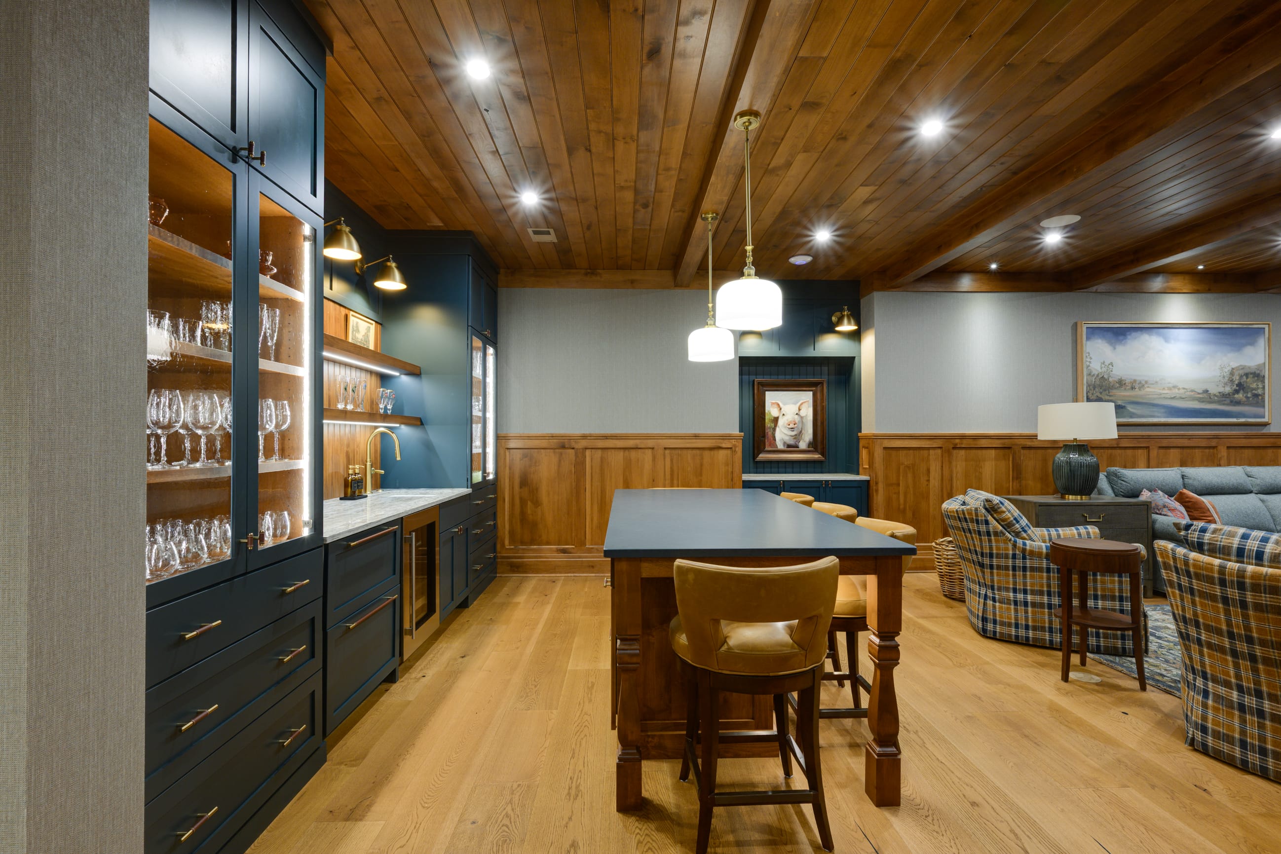 Stylish bar area with blue cabinetry, glassware, wooden accents, and cozy seating featuring plaid patterns.