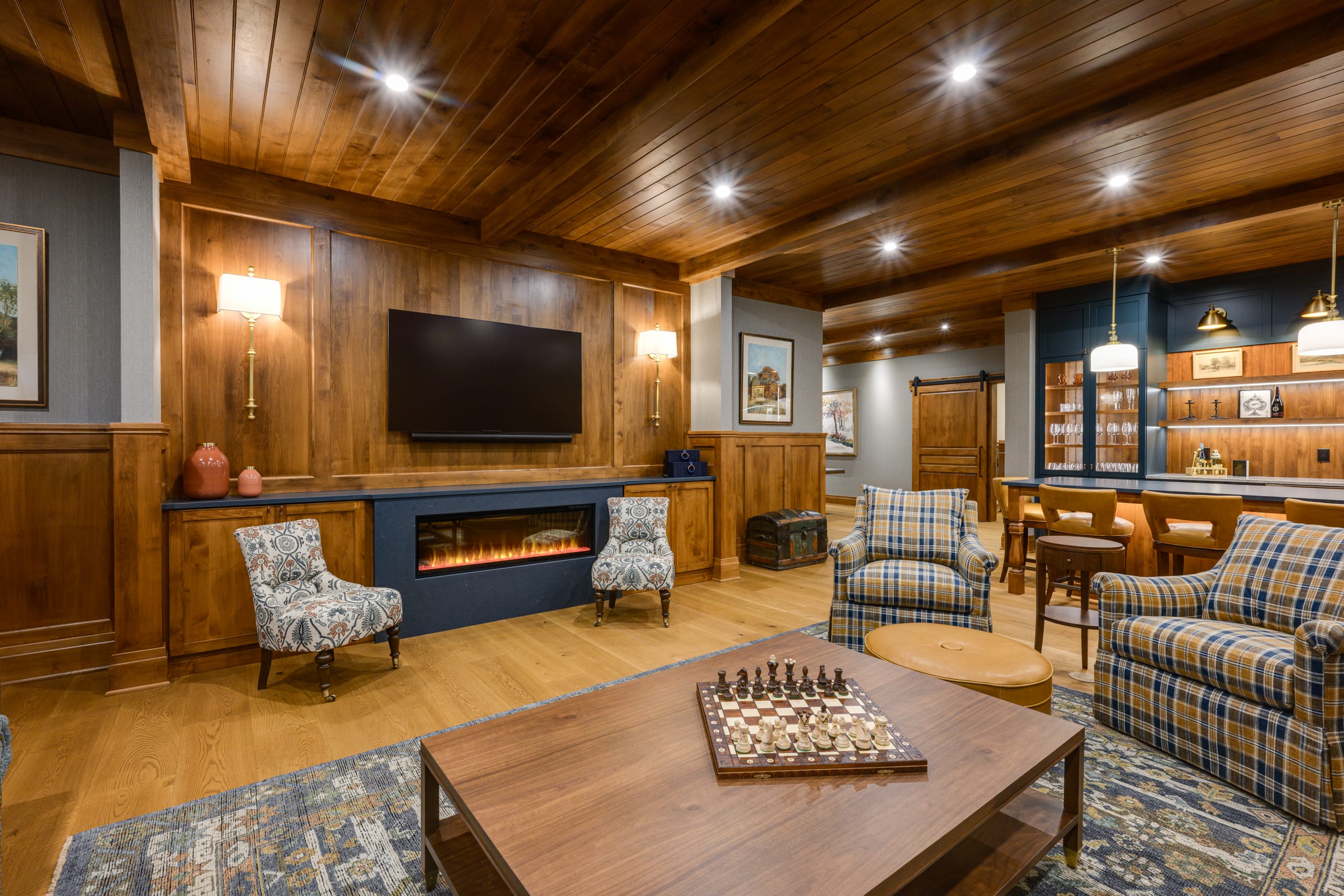 Cozy living room featuring a fireplace, wooden accents, plaid chairs, and a chess set on a coffee table.