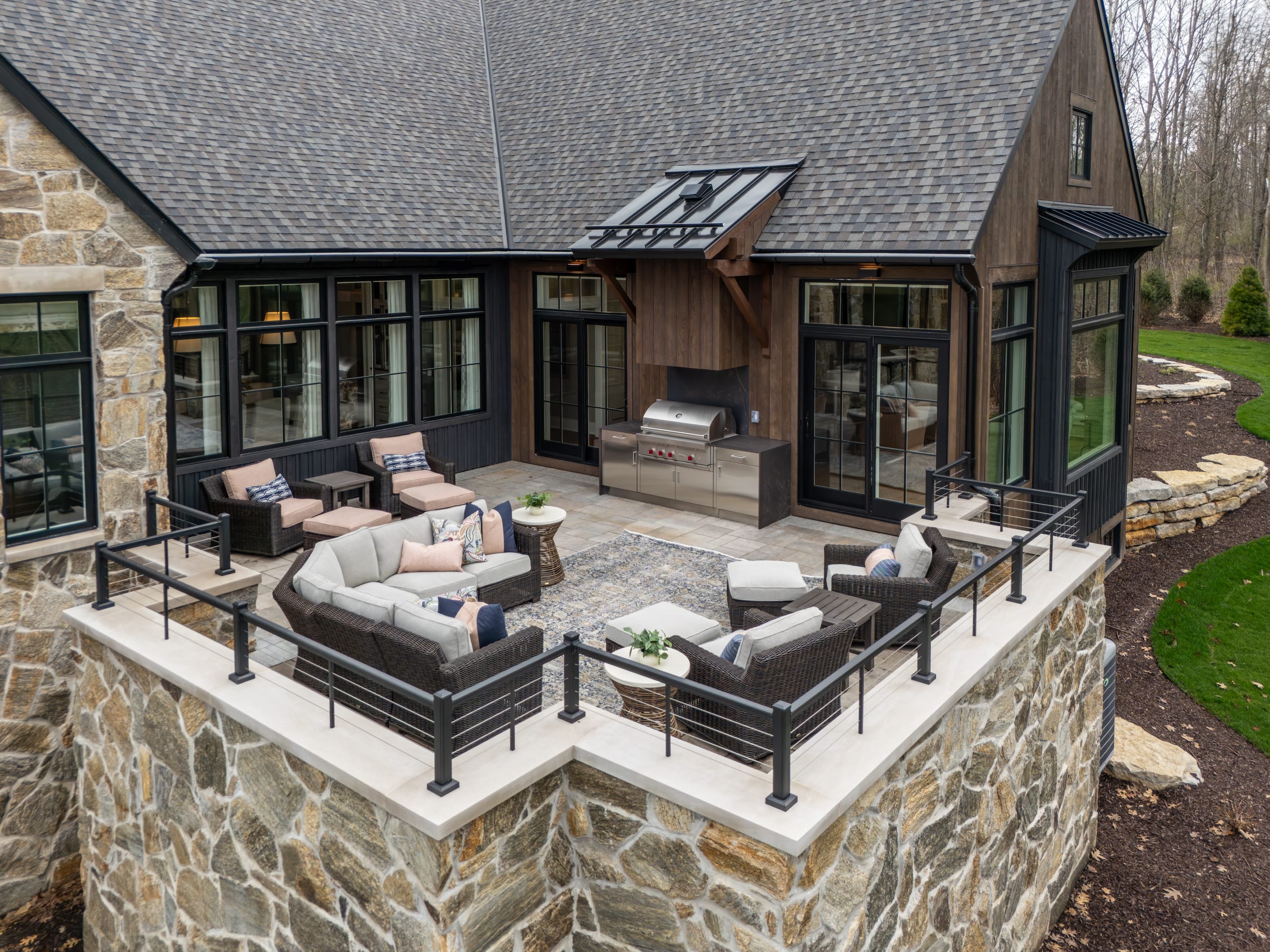 Stylish outdoor patio with seating, a grill, and a stone wall, surrounded by greenery and modern architecture.