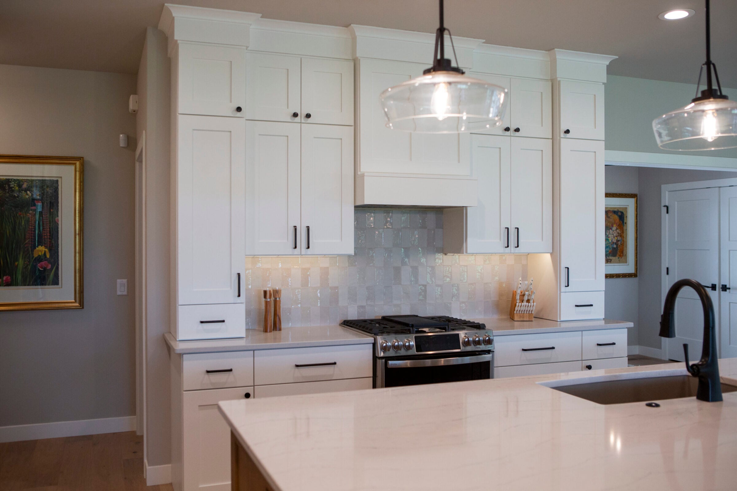 Modern white kitchen with stainless steel gas range and black faucet.