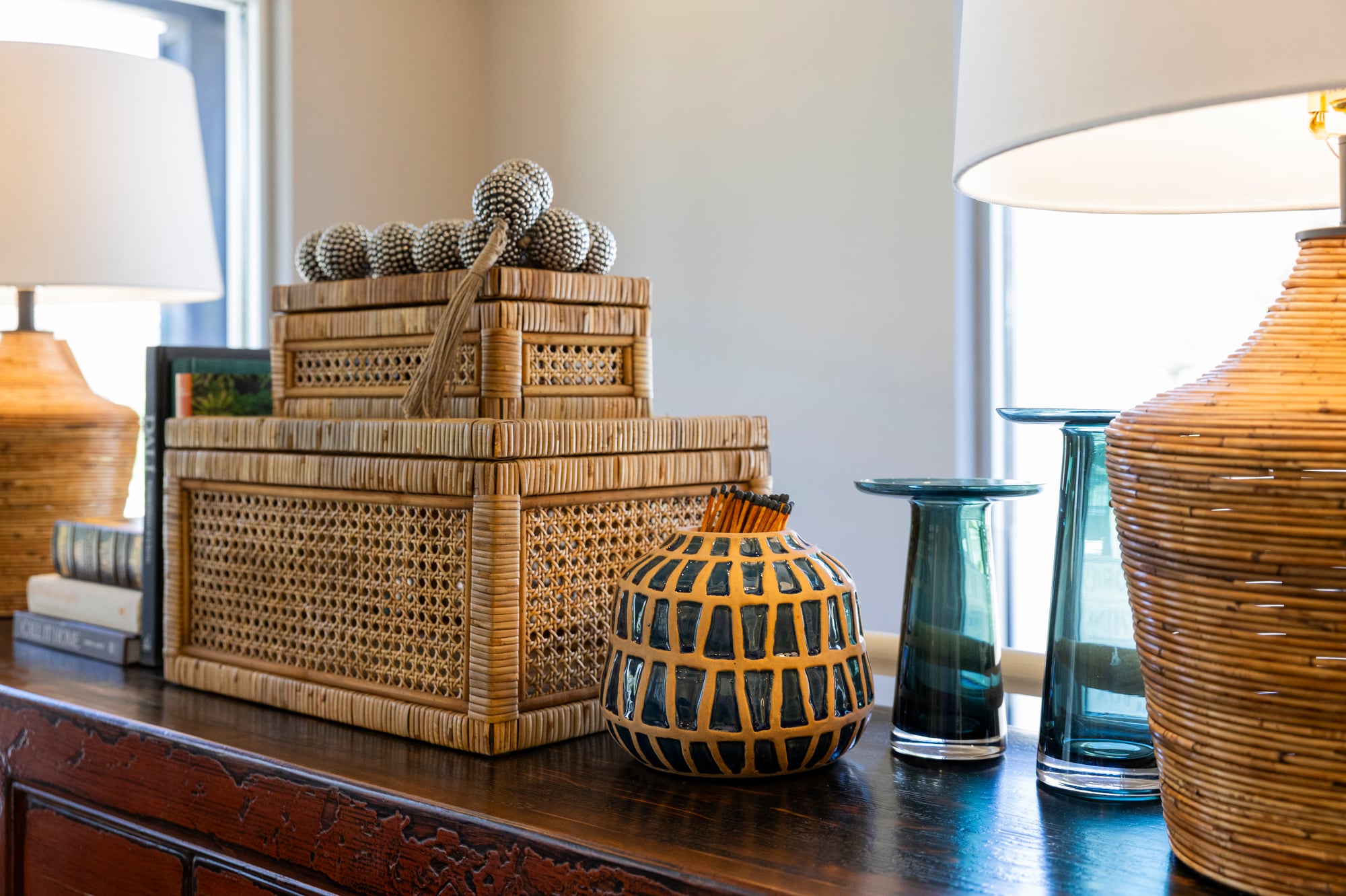 Woven rattan boxes topped with decorative spheres, a patterned vase with matches, and blue glass vases on a dark wood surface.