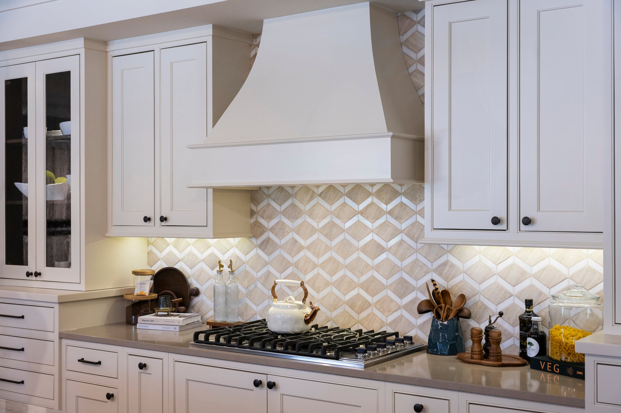 Kitchen with white cabinets, patterned backsplash, and a gas stovetop with a white teapot.