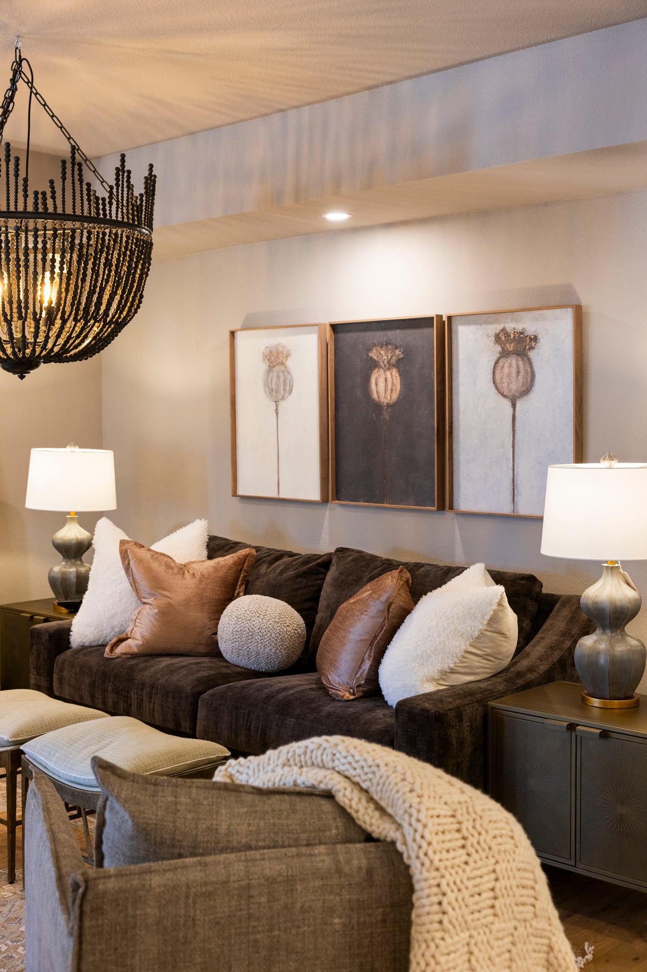 Dark brown sofa with textured pillows, three framed poppy art pieces, and a beaded chandelier.