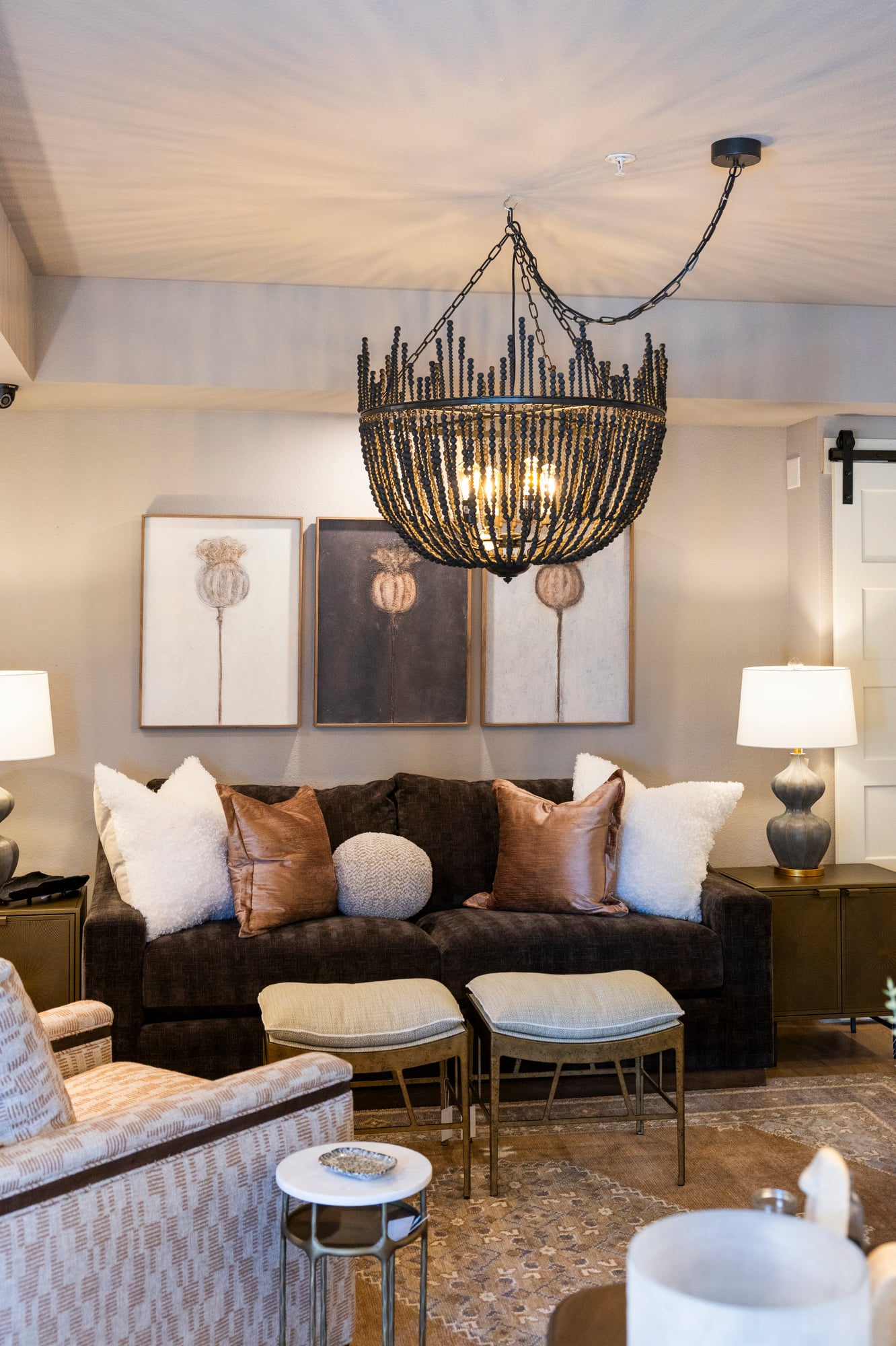 Dark brown sofa with decorative pillows, three botanical prints, and a beaded chandelier.