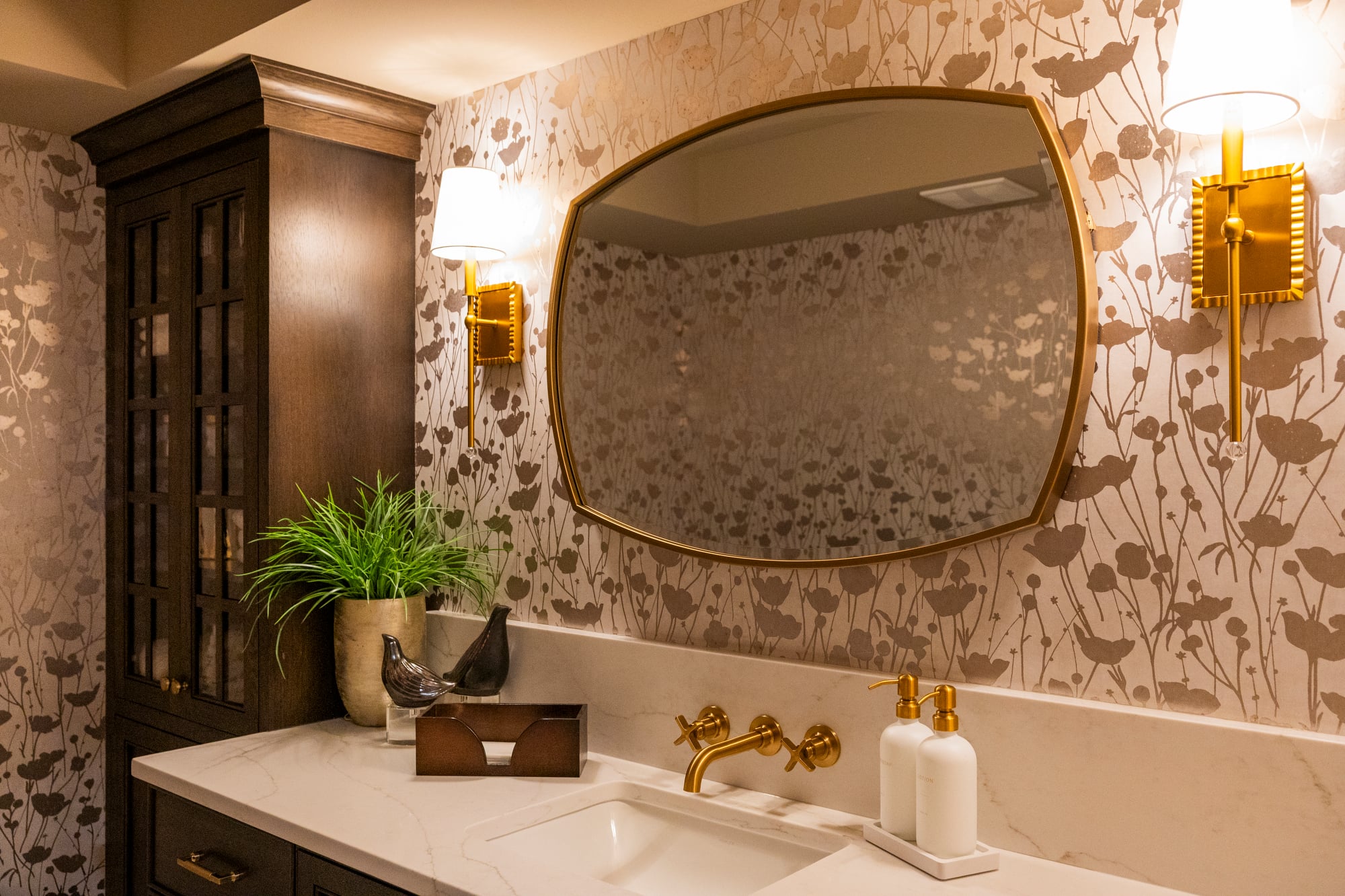 Bathroom vanity with a floral wallpaper, oval mirror, and gold fixtures.