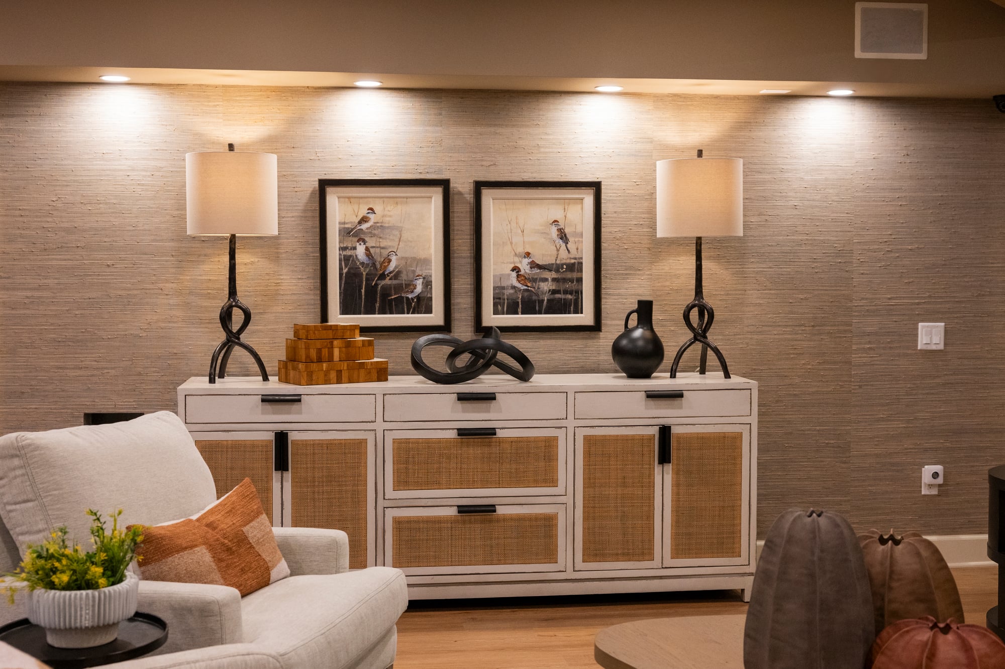 White sideboard with cane doors, flanked by lamps and bird art.
