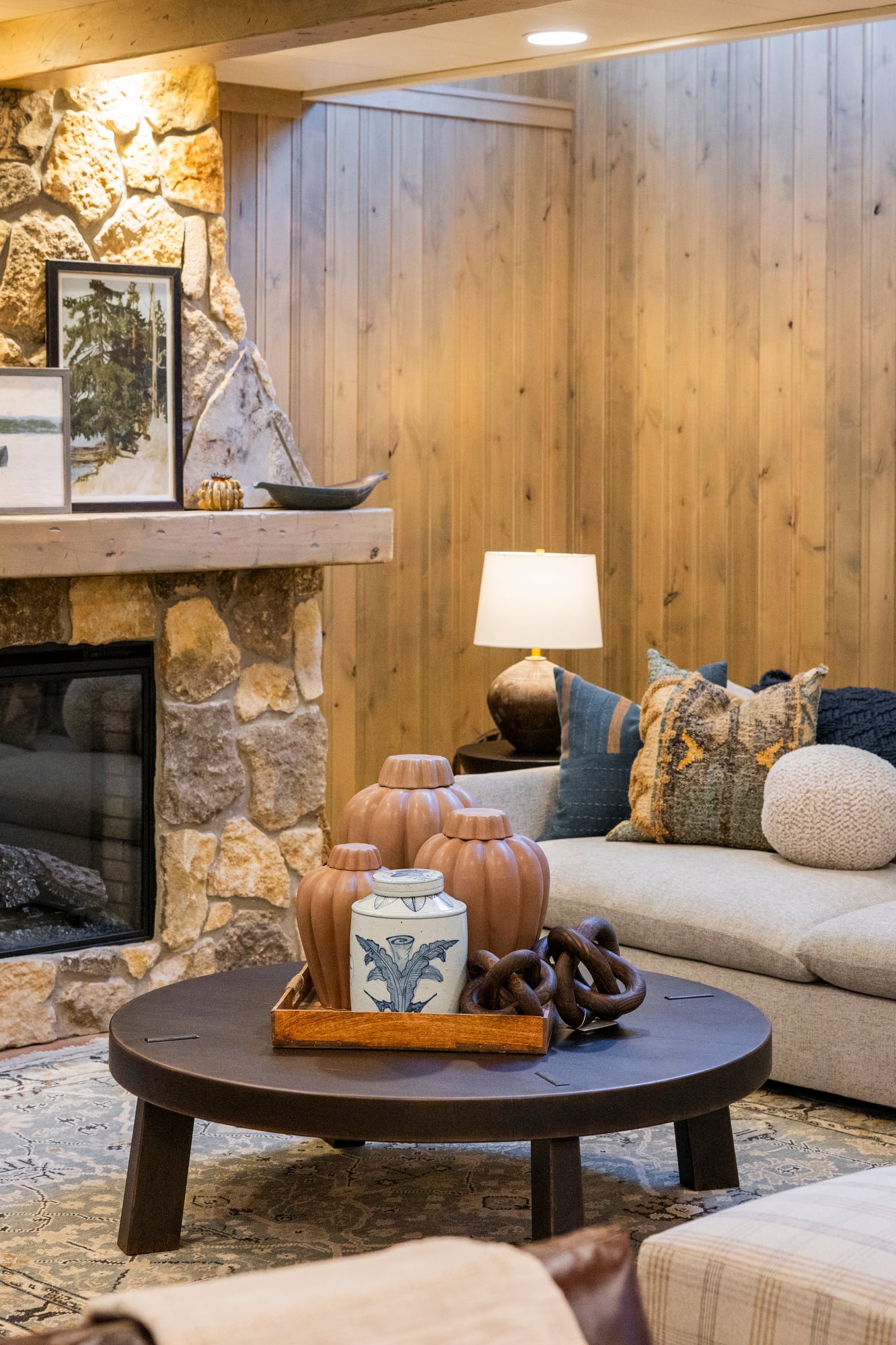 Living room with stone fireplace, wood paneling, and a coffee table with decorative vases.