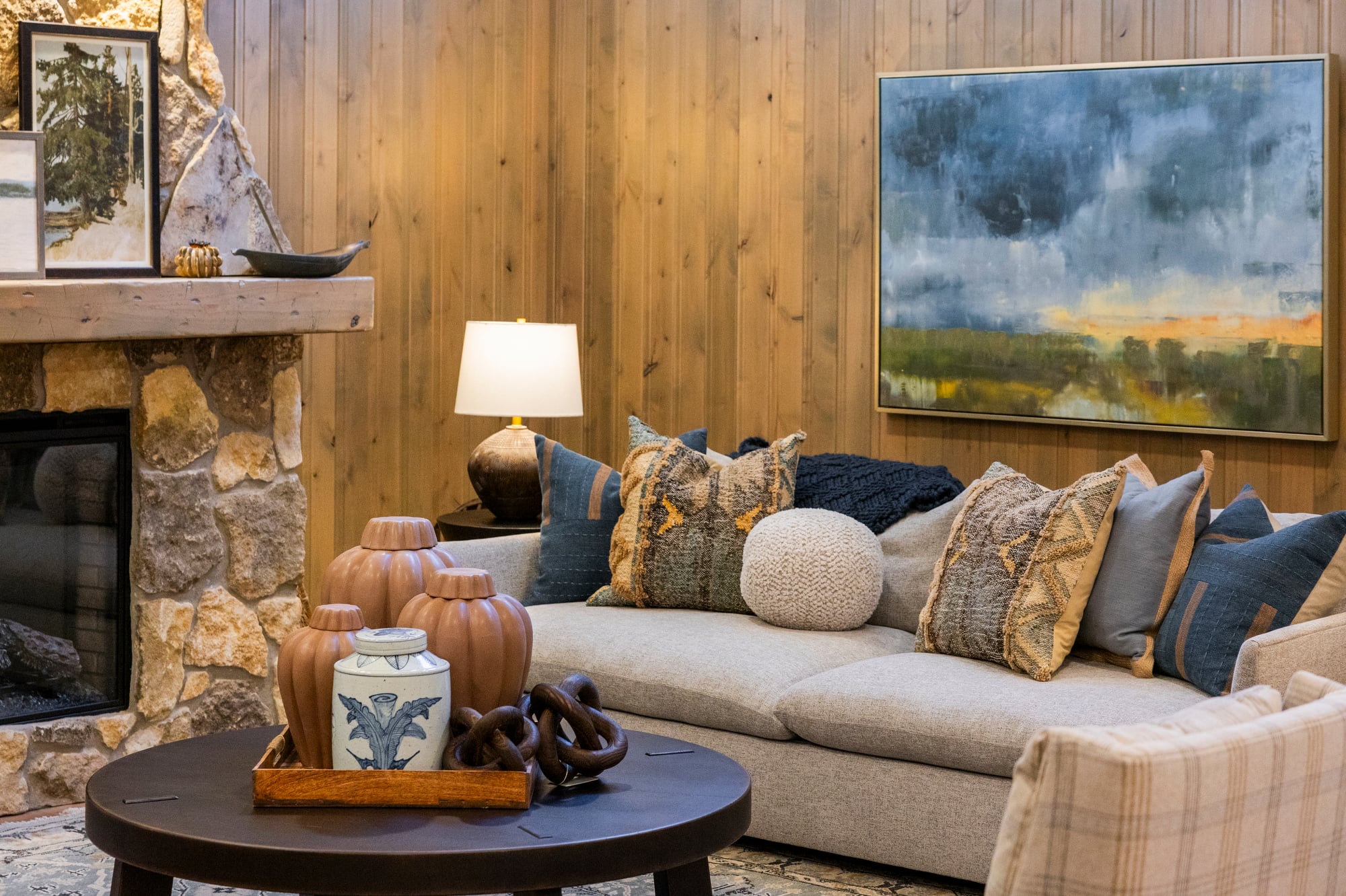 Cozy living room with stone fireplace, wood paneling, and a sofa with patterned pillows.