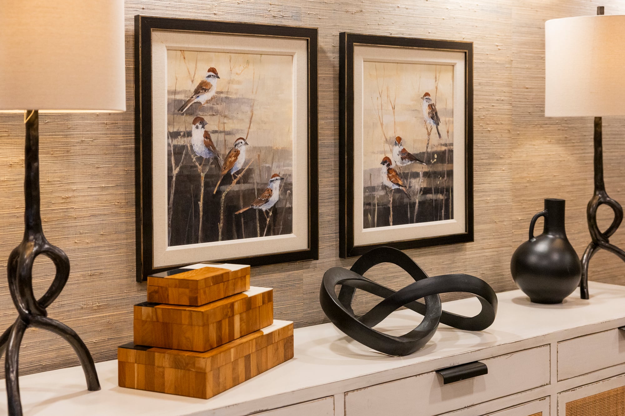 Two framed paintings of birds on branches, with decorative boxes and sculptures on a console table.
