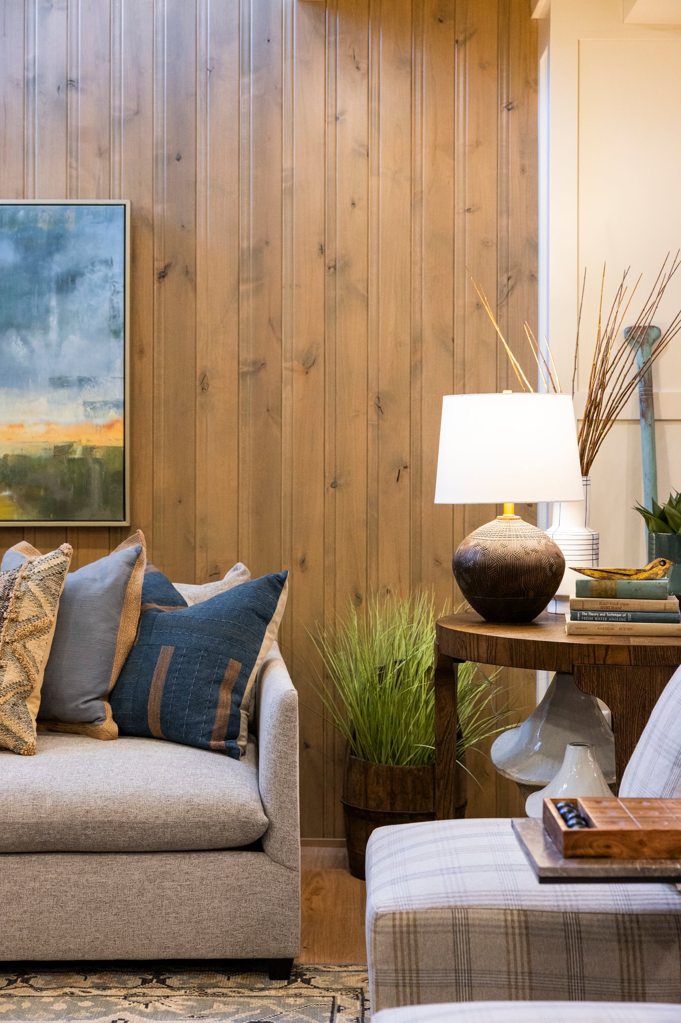 Sofa with patterned pillows, lamp on a side table, and artwork on a wood-paneled wall.