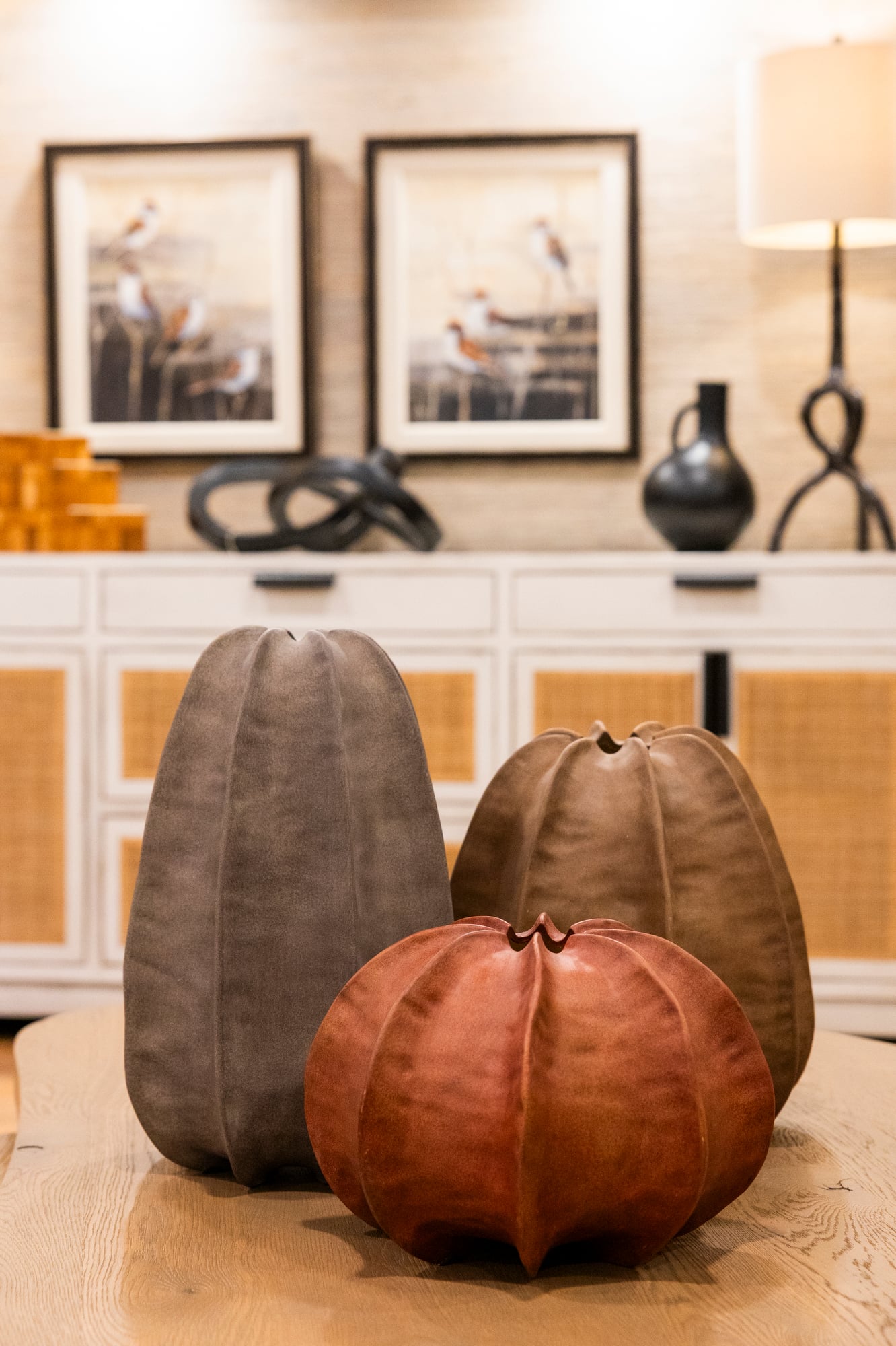 Three textured, gourd-shaped decorative objects in rust, brown, and gray on a wooden table.