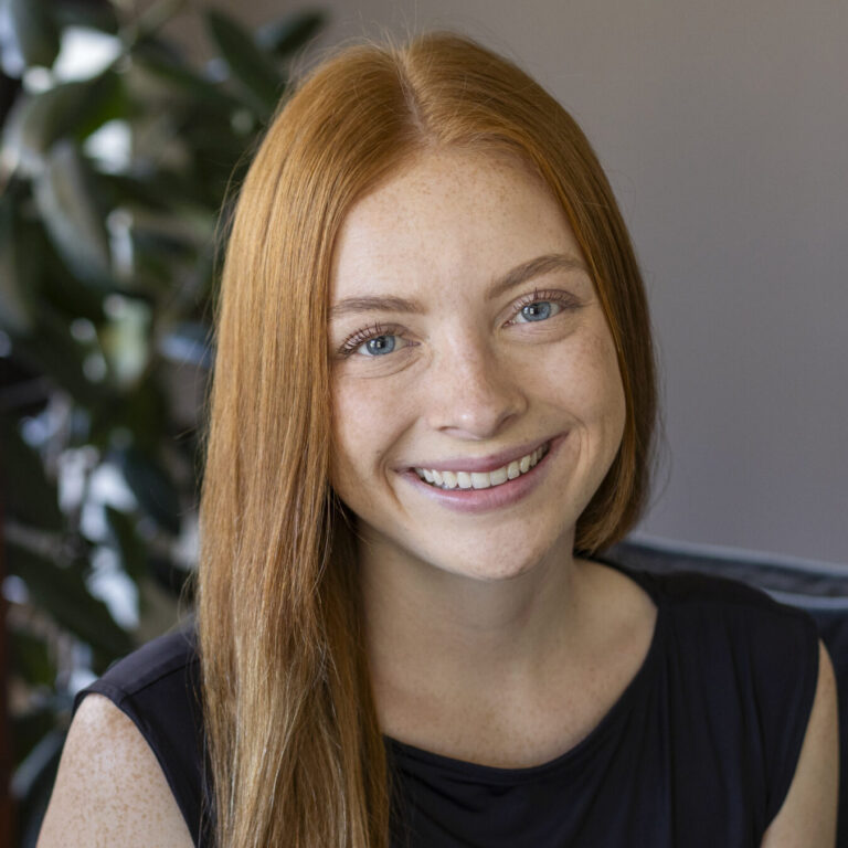 Woman with red hair and blue eyes smiling, wearing a black shirt.