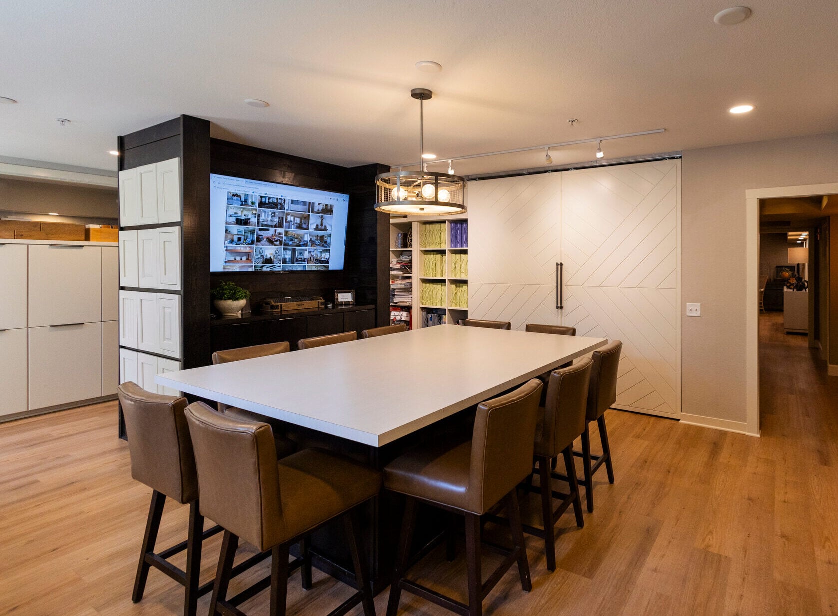Large conference table with leather stools, facing a wall-mounted TV displaying a collage of images.