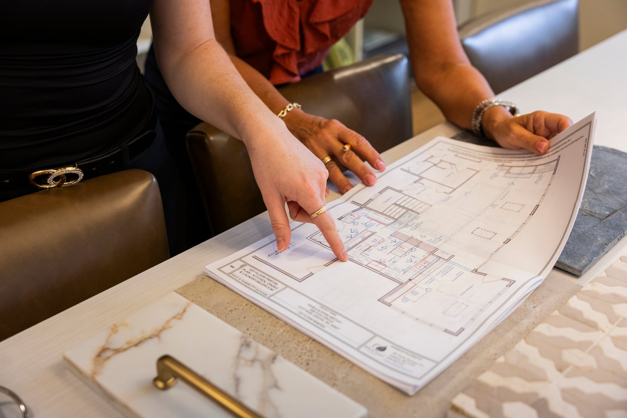 Two women review architectural plans and material samples on a table.