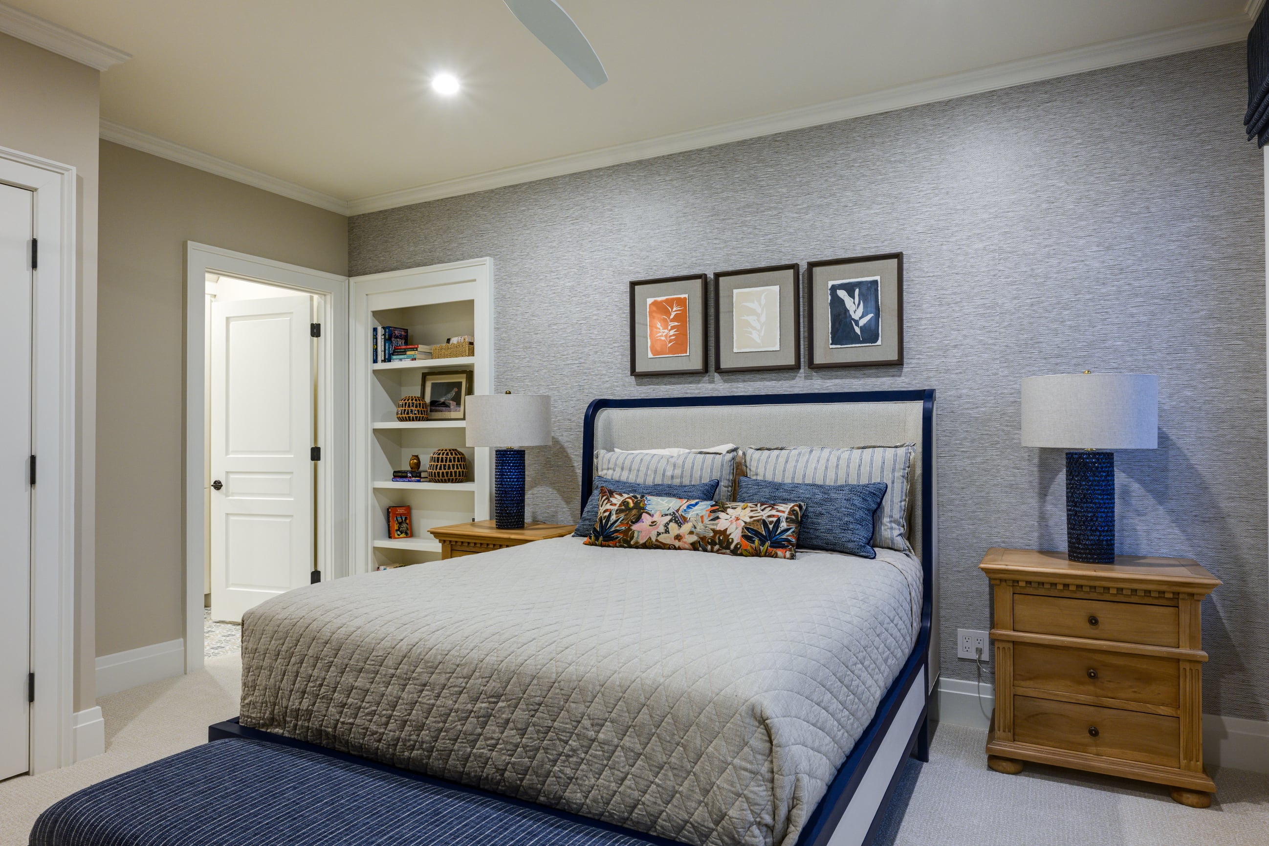 Bedroom with a quilted bed, patterned wallpaper, and three framed art pieces.