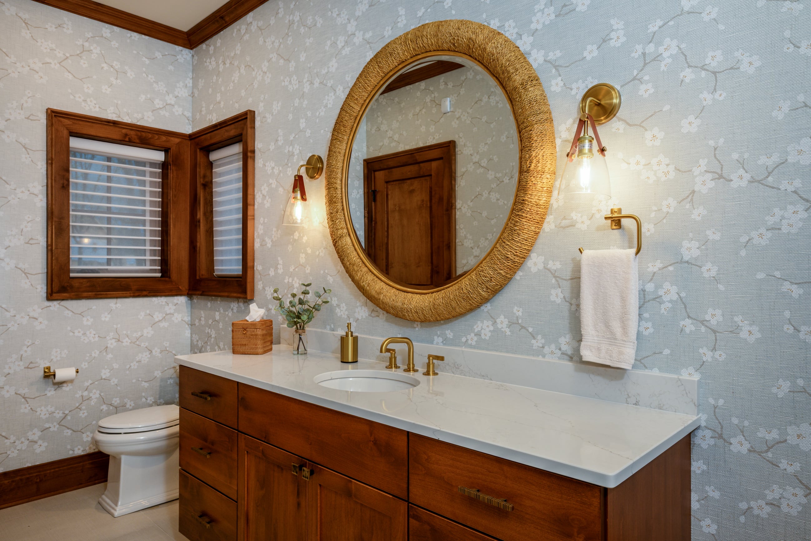 Bathroom vanity with floral wallpaper, oval mirror, and wooden window.
